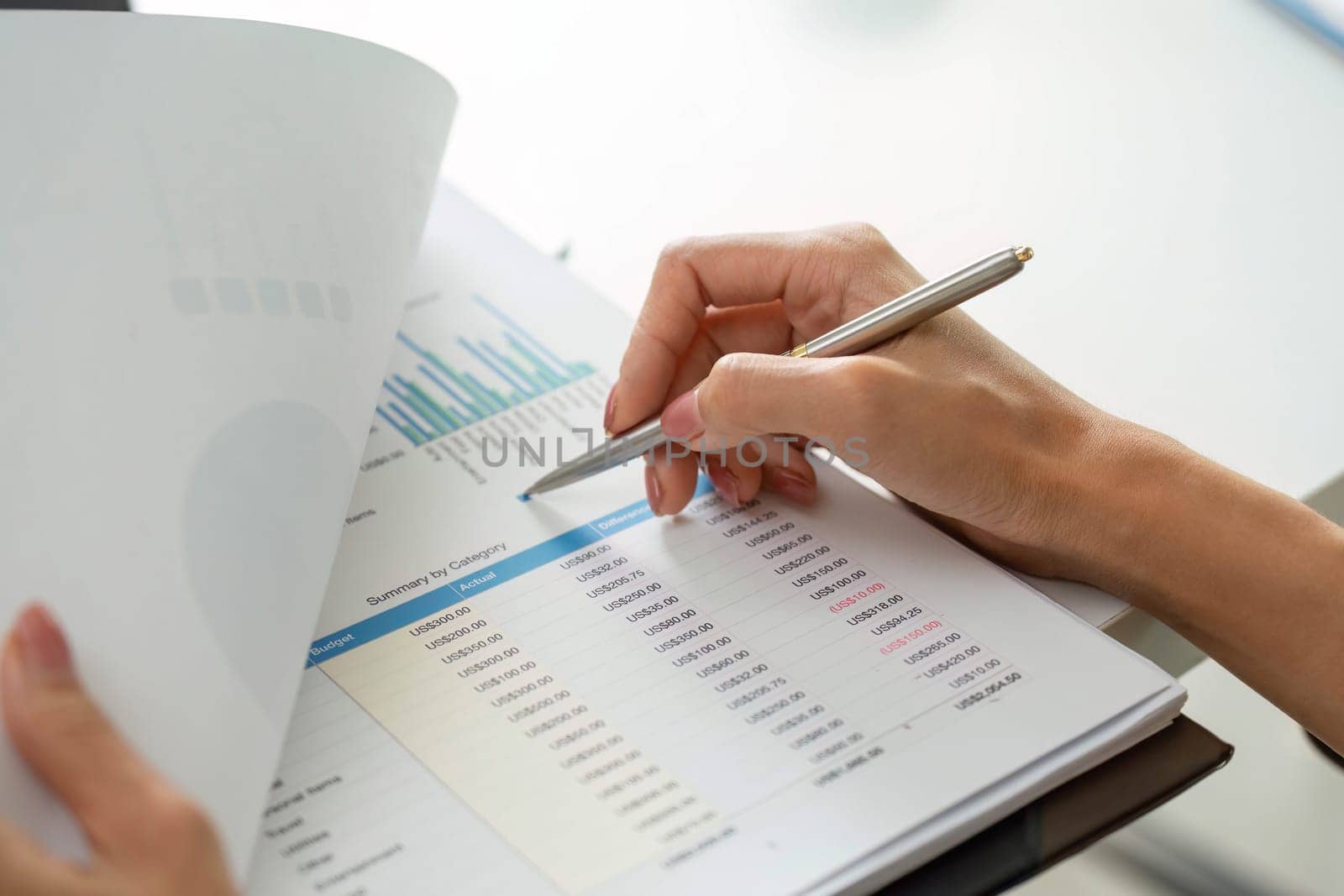 Dedicated to analyzing her report, a woman closely inspects financial data, noting important trends and insights as she prepares for an upcoming presentation.