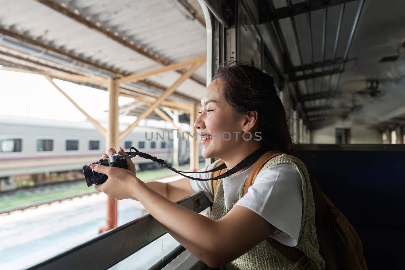 With a camera in hand, a young woman captures the beautiful scenery outside her train window, celebrating travel and adventure.