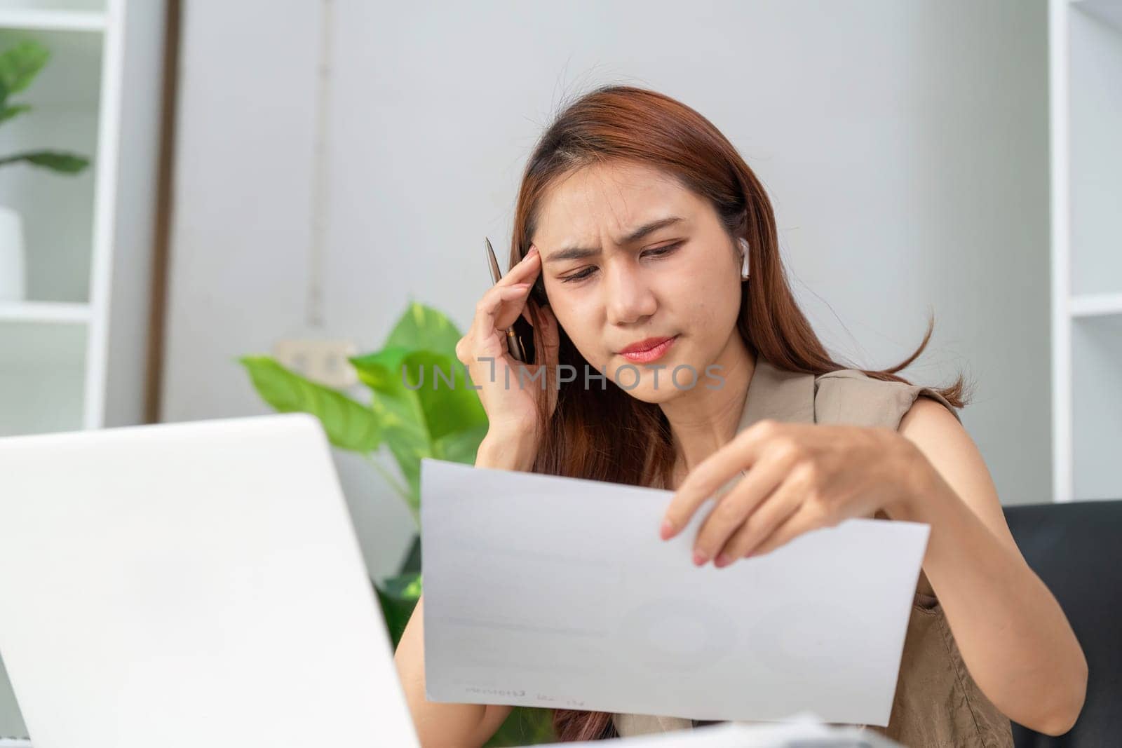 In a moment of stress, a woman examines paperwork while on a call, highlighting the pressures of managing data and tasks efficiently.