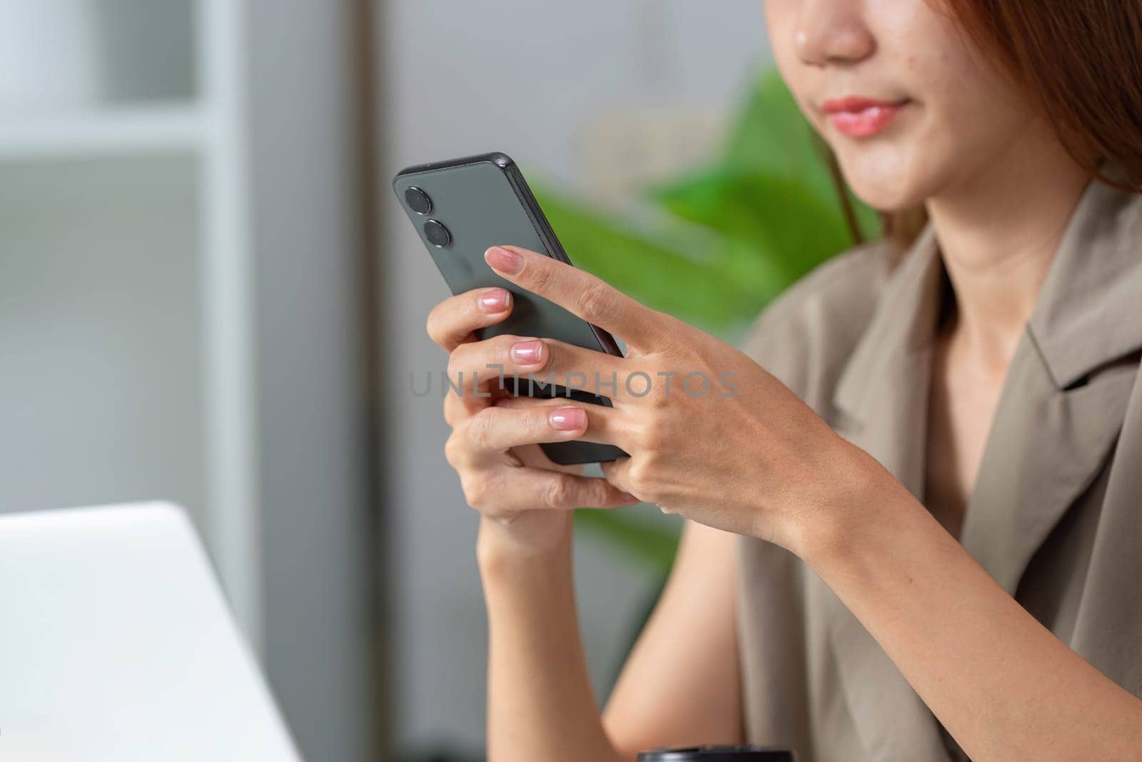 A woman focuses on her smartphone, signifying the integration of mobile technology in daily work routines and communication.