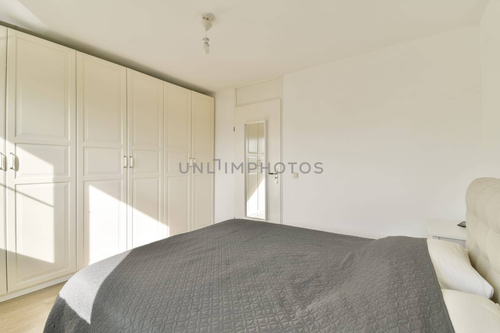 A bright and spacious modern bedroom featuring minimalistic design with white cabinetry and a comfortable bed dressed in gray linens. Ideal for contemporary living.