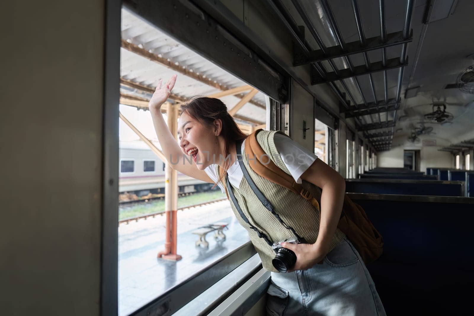 Waving enthusiastically from the window of a train, a young woman captures the spirit of adventure and exploration during her journey.