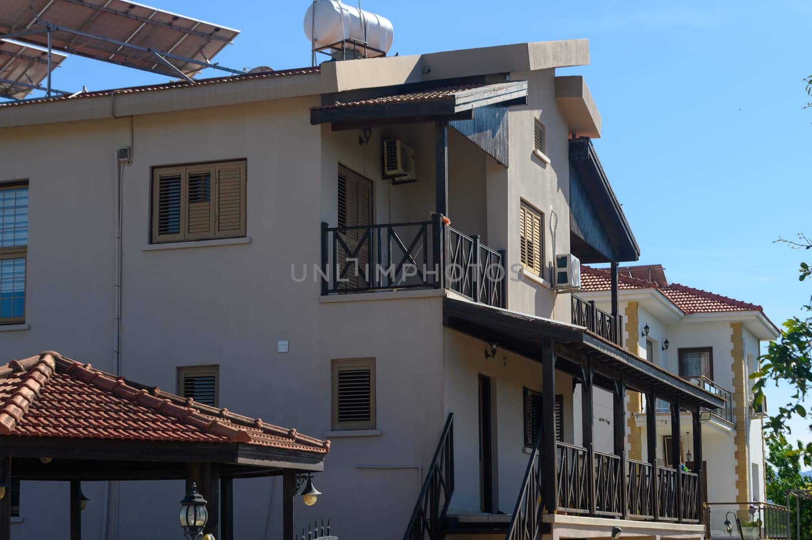 Basking in warm sunlight, this elegant residential structure features a spacious balcony, showcases architectural details, and is framed by vibrant greenery enhancing its inviting atmosphere.