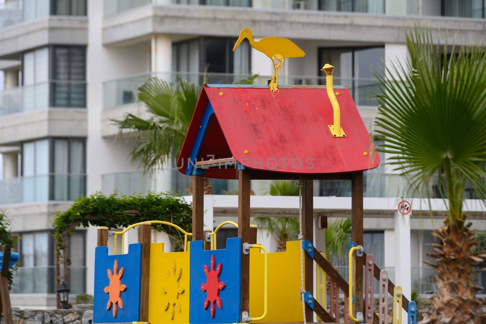 A vibrant playground structure featuring playful designs sits beneath tall palm trees beside a sleek apartment building. The cheerful colors invite children to explore and create fun memories.