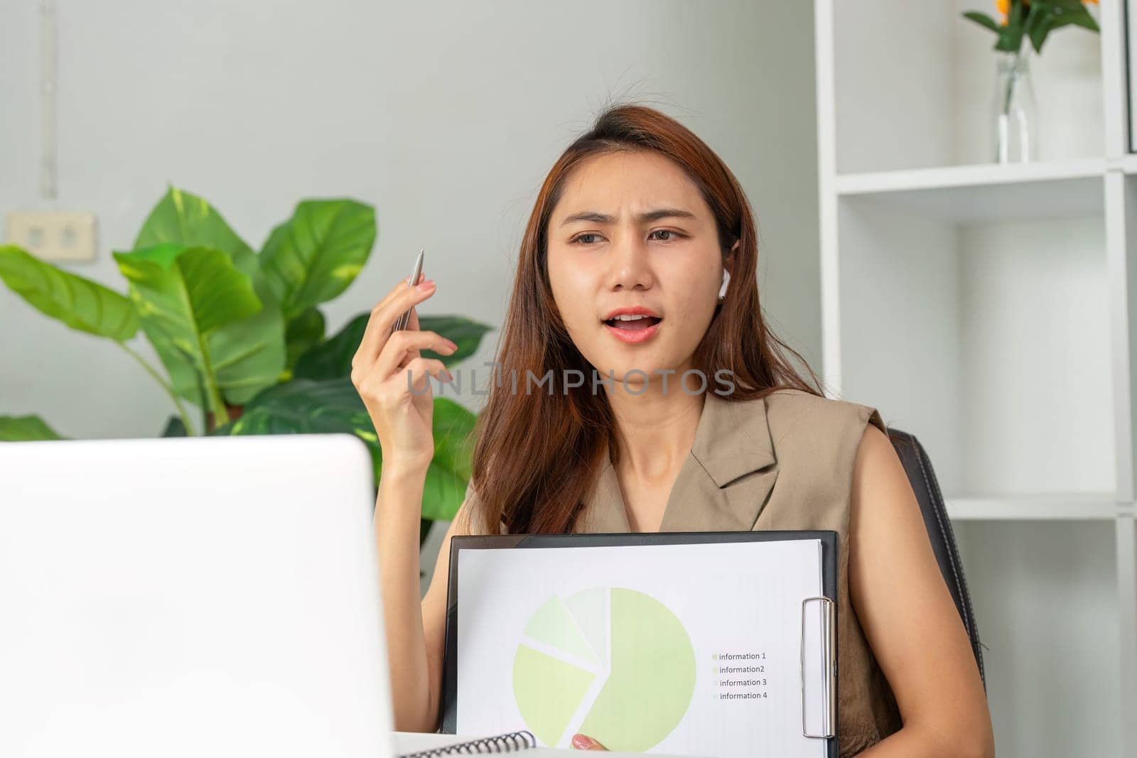 In a contemporary workspace, a young professional uses video conferencing to share her analytical insights, gesturing toward a pie chart to illustrate her key points.