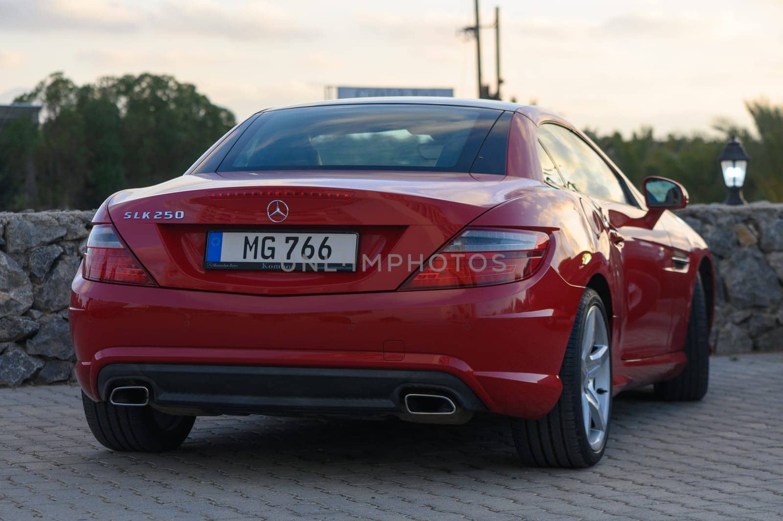 Gaziveren Cyprus -16.04.2025 A stunning red sports car stands gracefully against a picturesque sunset backdrop. The sun casts a soft glow, showcasing the car's glossy finish and elegant lines as it relaxes by a tranquil setting.