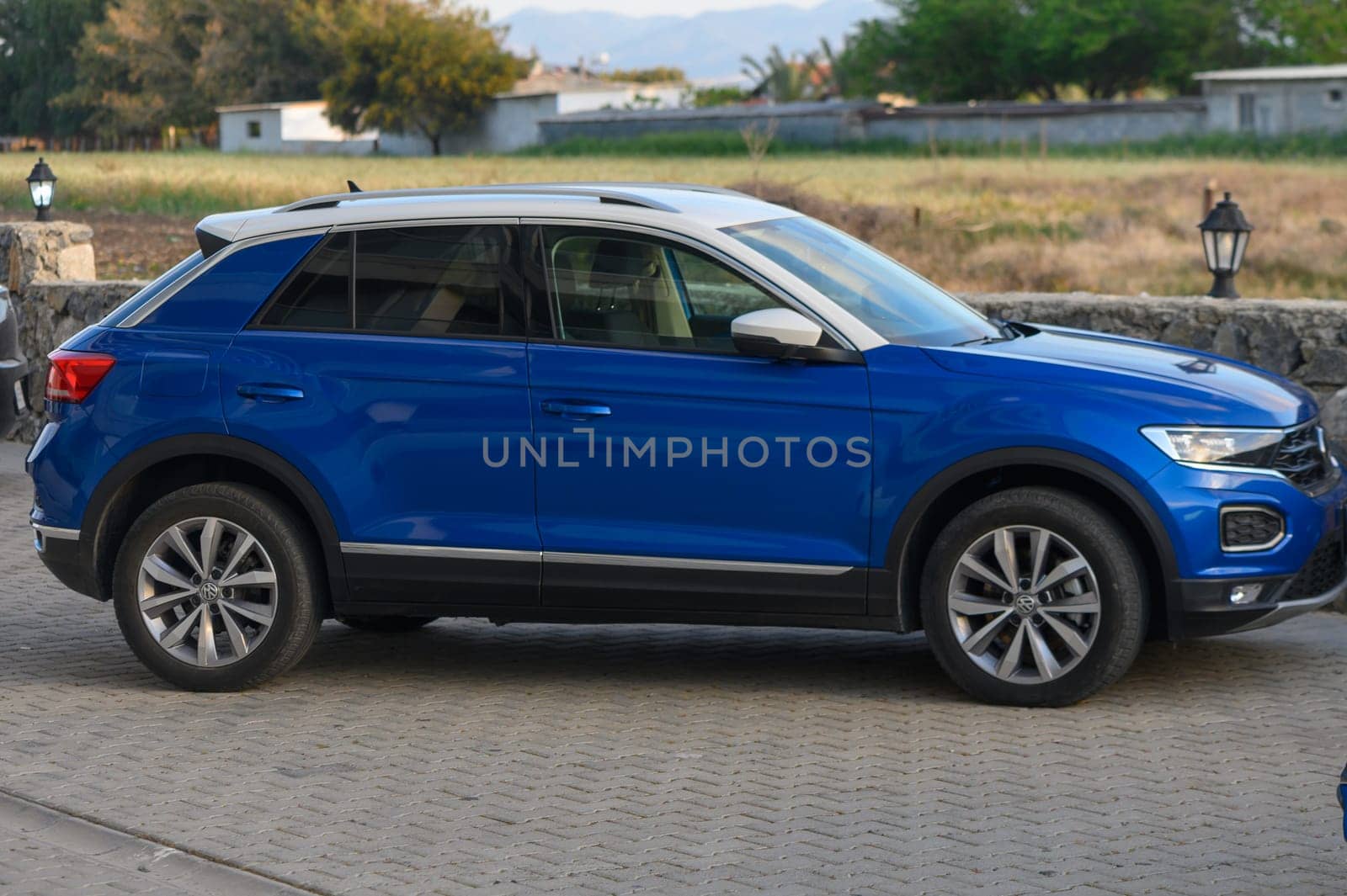 Gaziveren Cyprus -16.04.2025 A vibrant blue SUV rests elegantly on a cobblestone surface, with lush green fields and distant trees painting a serene picture of tranquility in the countryside.