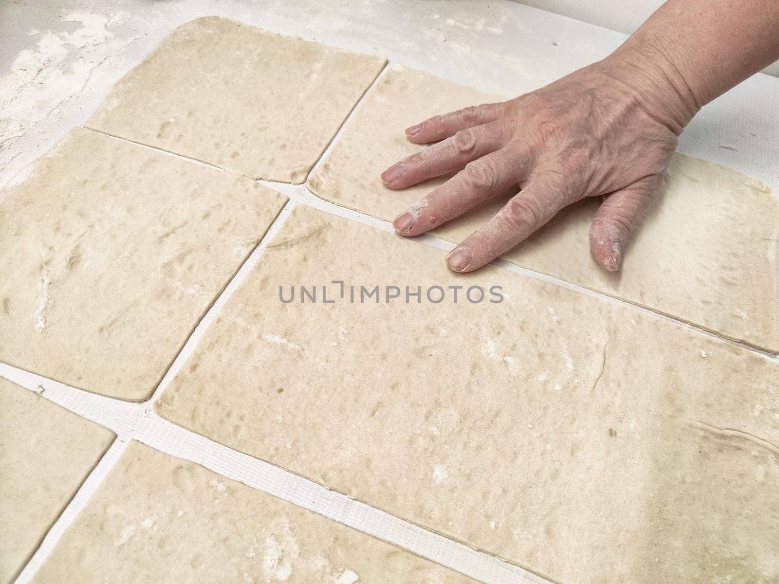 A hand presses down on freshly rolled dough, dividing it into even rectangular pieces on a clean work surface in a bright kitchen.