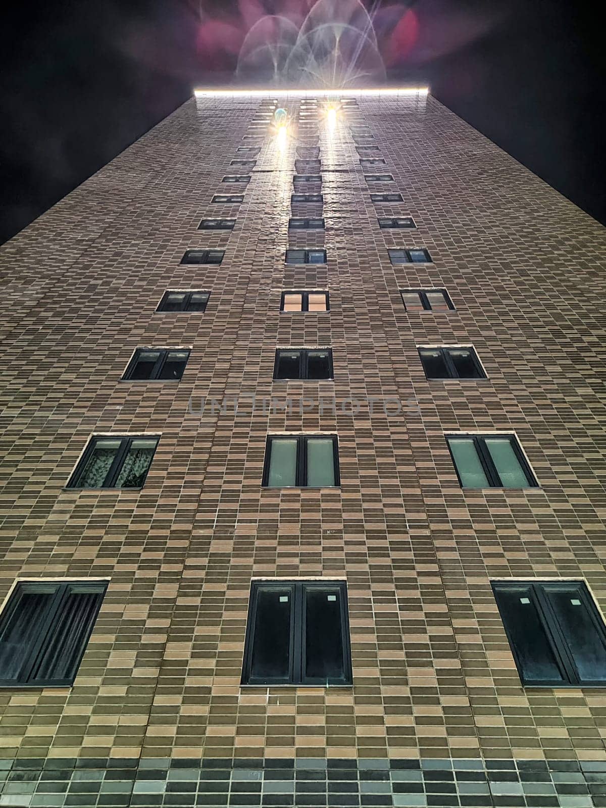 A towering structure stands illuminated during the night, surrounded by a clear sky, showcasing its architectural design from a low perspective.