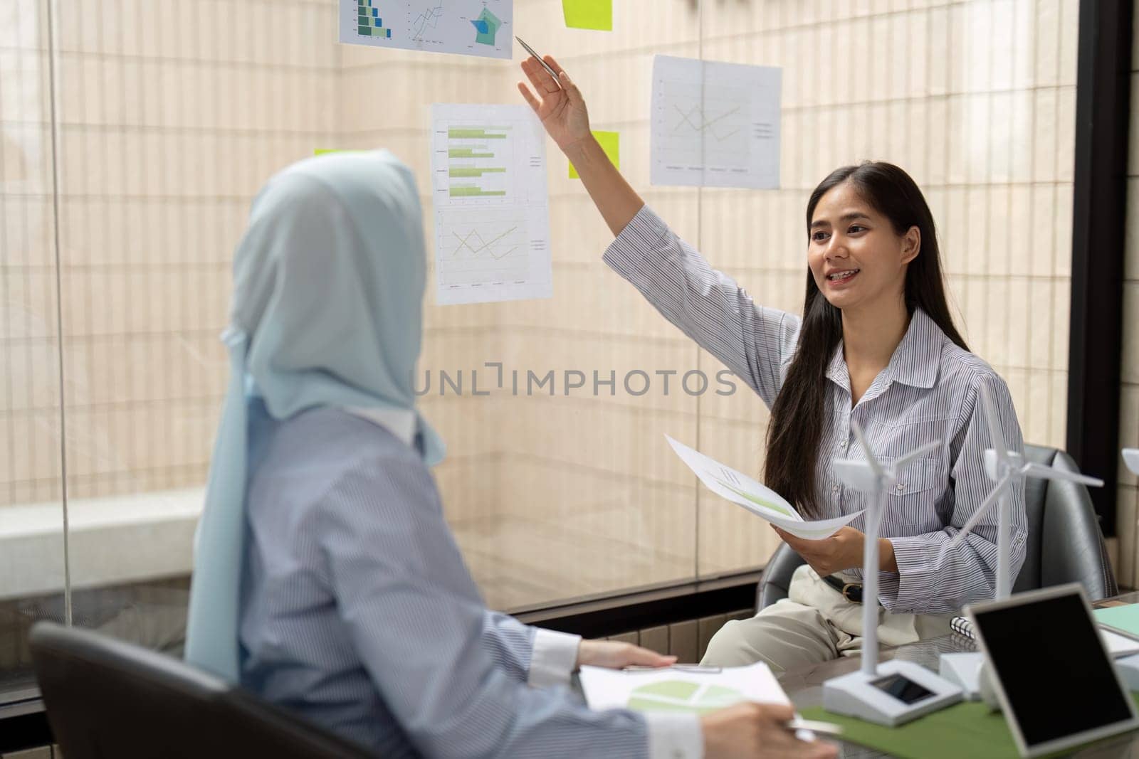 Leveraging visual aids, one woman passionately presents her ideas about sustainability initiatives, engaging her colleague in a dynamic discussion about implementation and impact.