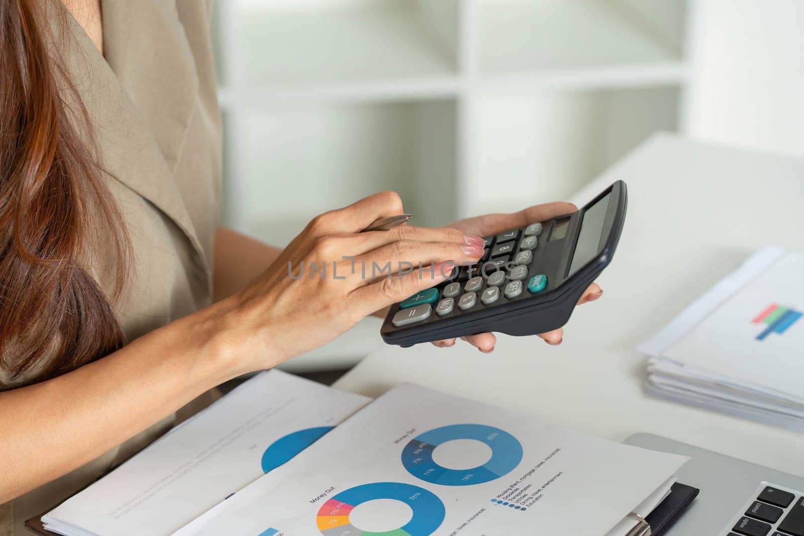 A focused woman uses a calculator while reviewing financial documents, demonstrating diligence in budget management and financial planning.