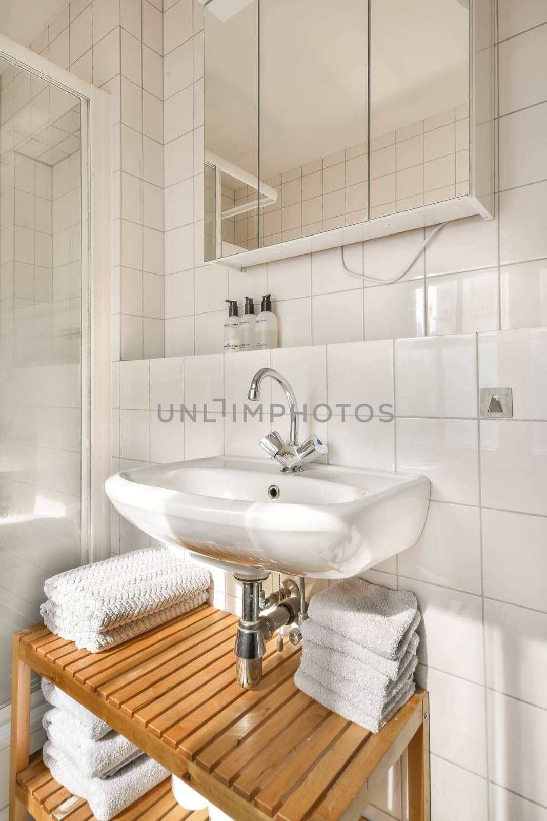 Stylish bathroom featuring a wooden shelf, a white sink, ample towels, and contemporary design elements in a bright setting.