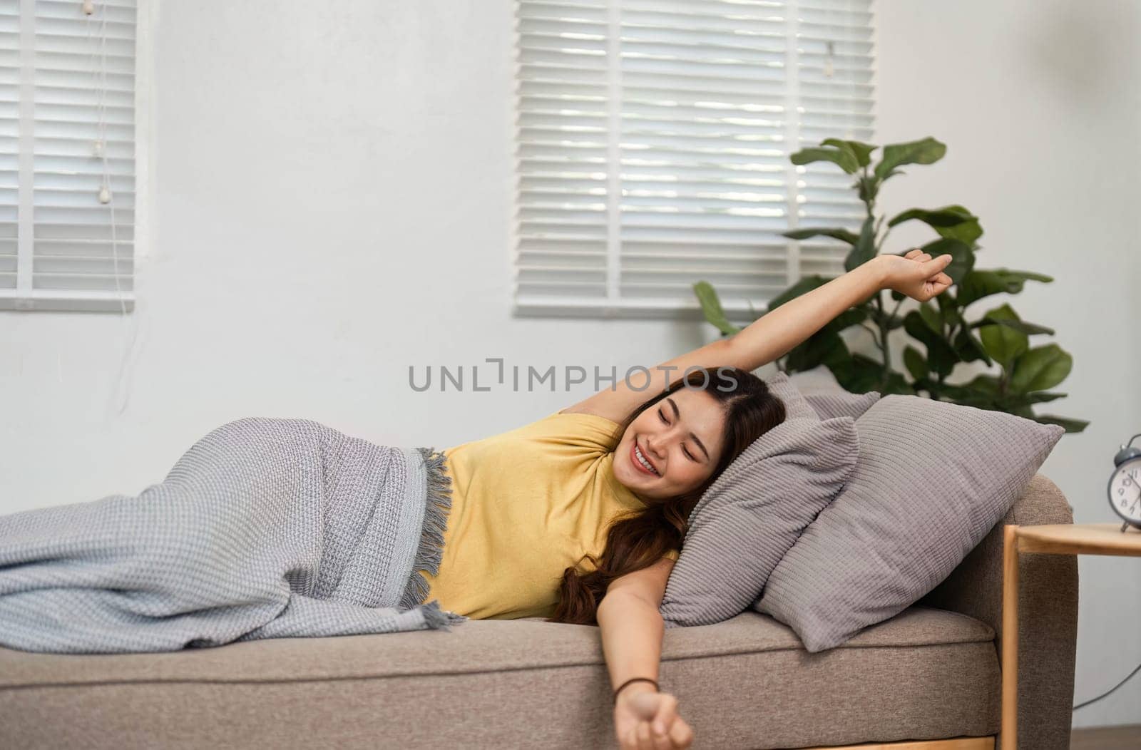 A young woman stretches her arms with a bright smile, enjoying the morning sun in her living room. This moment captures the happiness of starting the day with positivity.