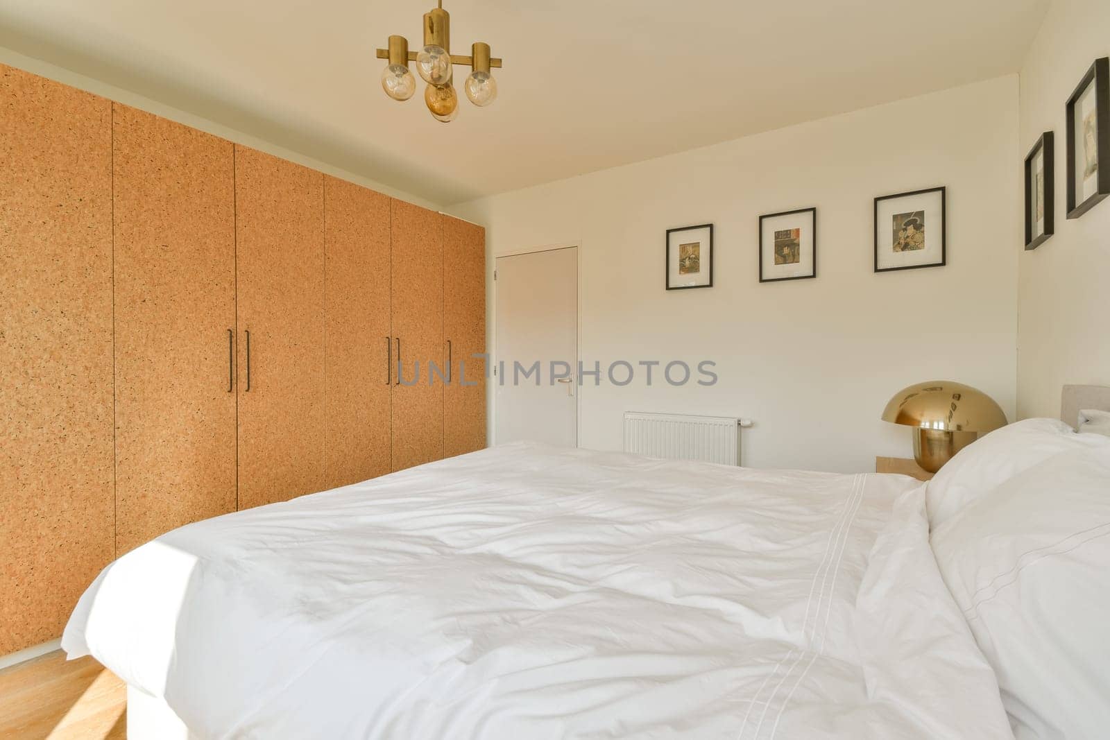 A stylish bedroom featuring a large bed, a wooden wardrobe, and decorative wall art, bathed in natural light for a serene atmosphere.