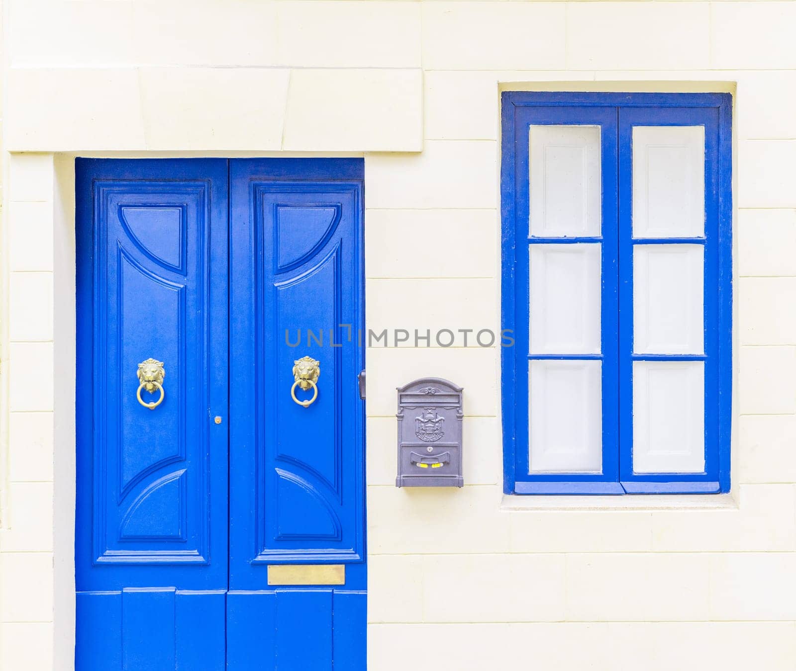 White brick wall with a blue window, door and a grey metal mail box.