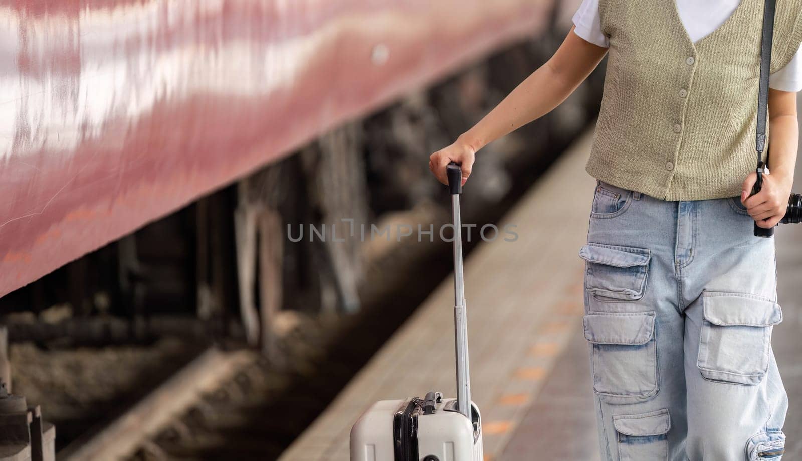 A young traveler is preparing for her journey by rolling her suitcase at the platform, showcasing personal style and organization while surrounded by the hustle of train travel.