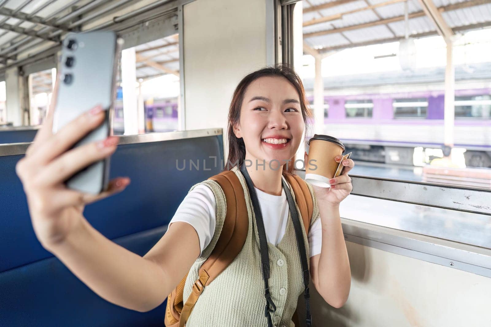 A young woman smiles brightly as she enjoys her coffee and snaps a selfie during a delightful train ride.