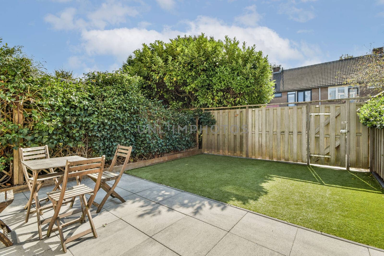 This backyard features lush greenery and a simple seating area, perfectly suited for relaxation and outdoor enjoyment, complete with artificial turf and wooden furniture.