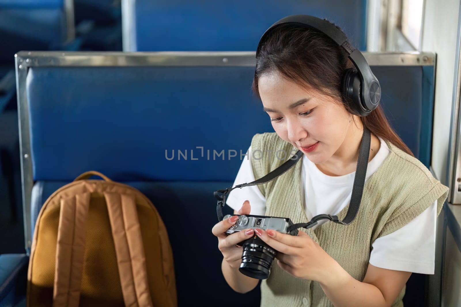 A young woman sits comfortably in a train, focused on her camera as she reviews photos, embodying the essence of a passionate photographer during her travels.