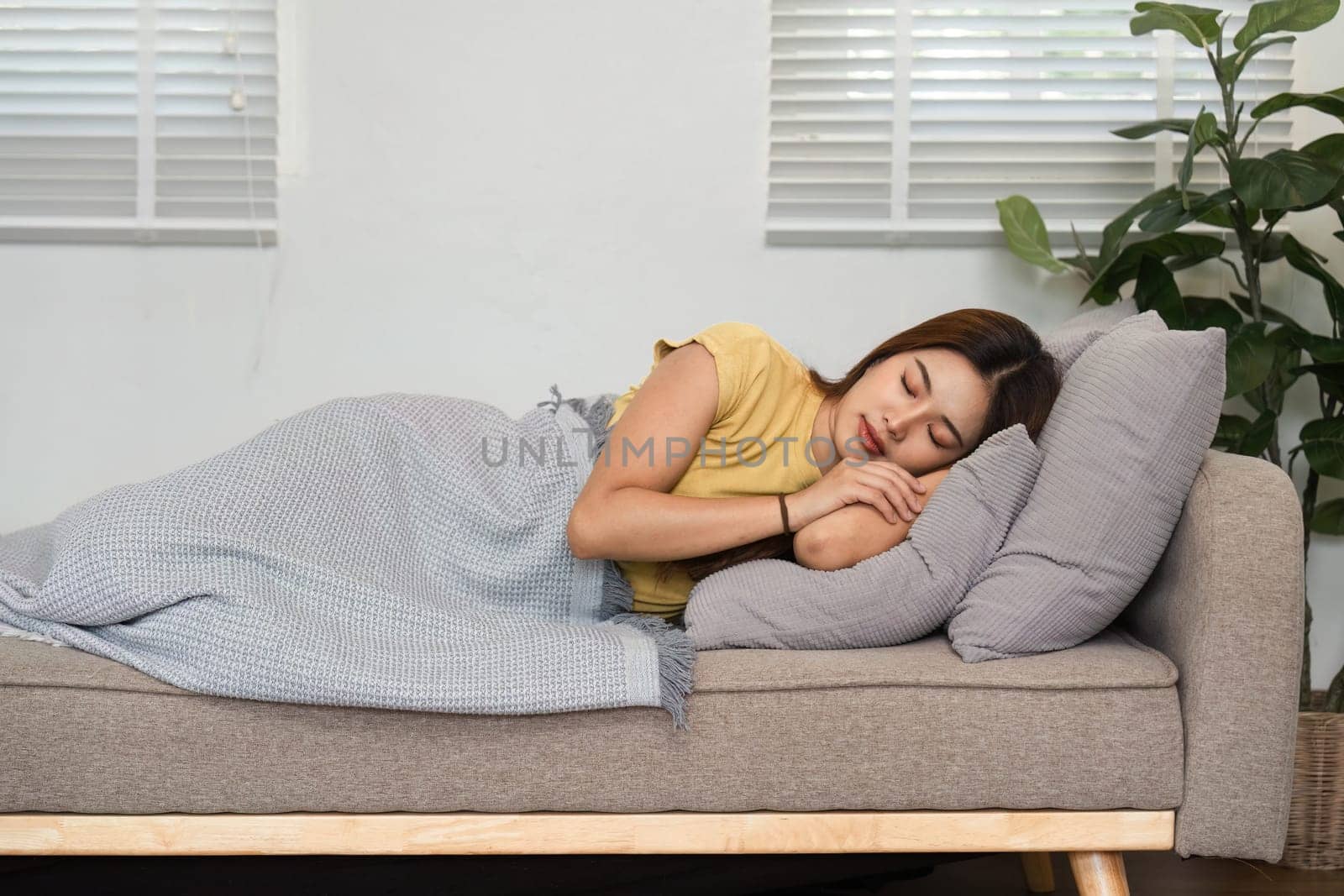 A young woman is sleeping soundly on a soft couch in a bright room, embodying the essence of a calm morning routine and relaxation.
