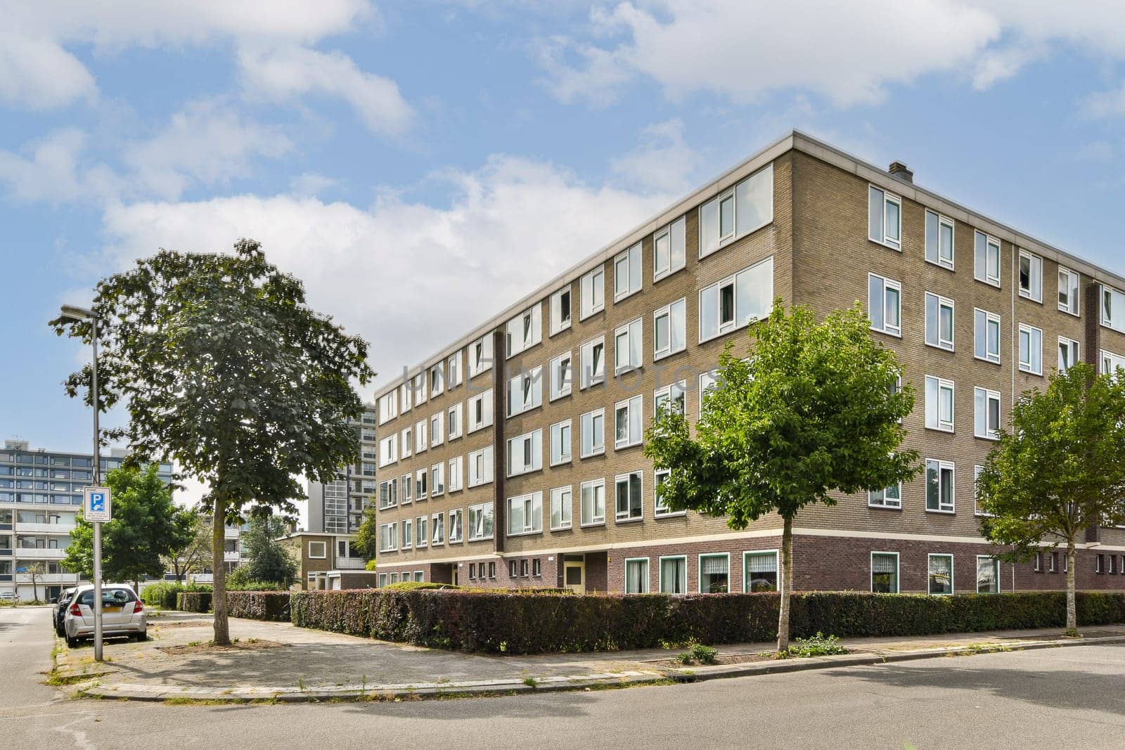 A modern residential building featuring large windows and greenery, set against a cloudy sky. The clean design enhances the urban landscape.