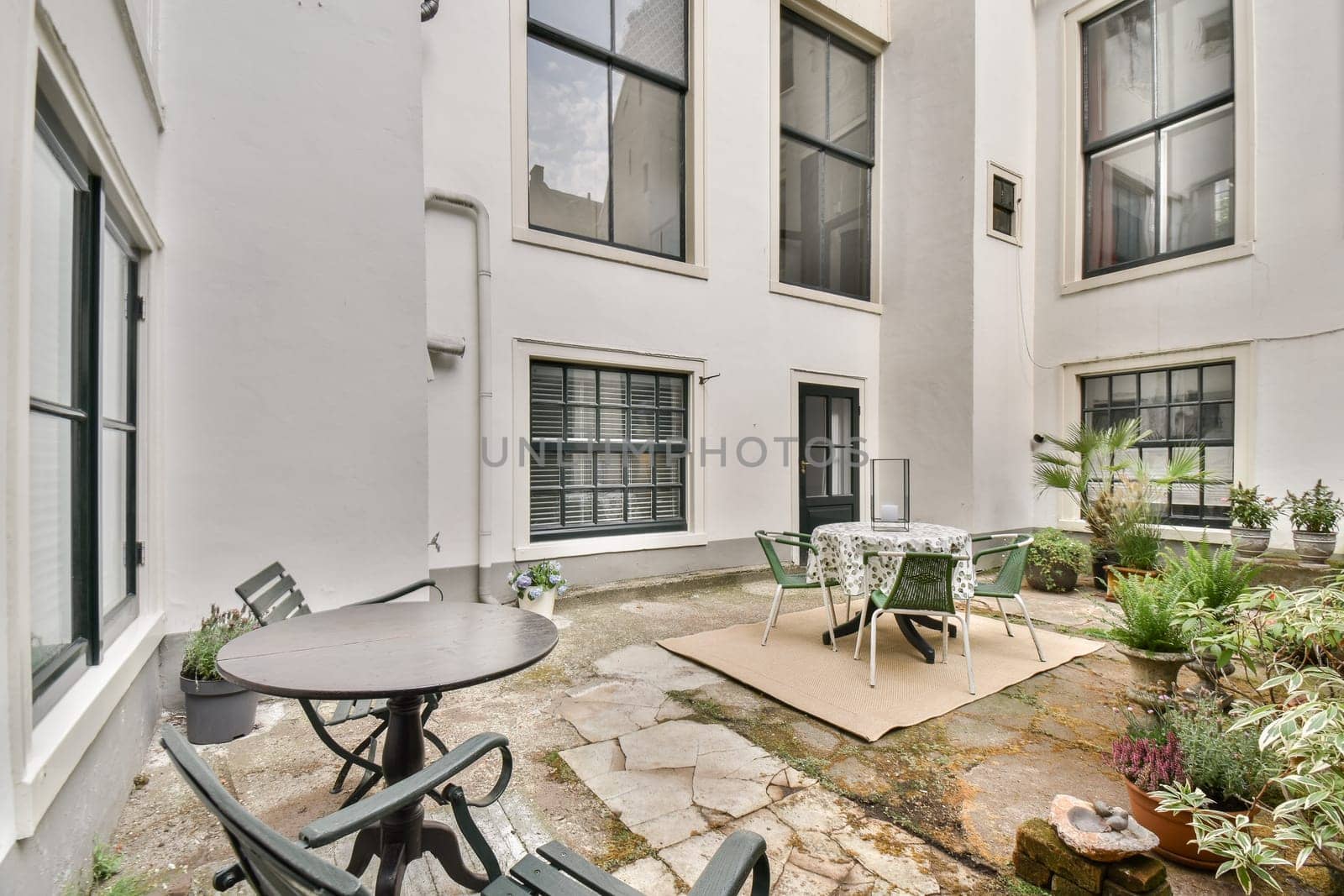 A serene courtyard featuring modern architecture, tables, chairs, and lush plants, providing a perfect spot for relaxation and gatherings.