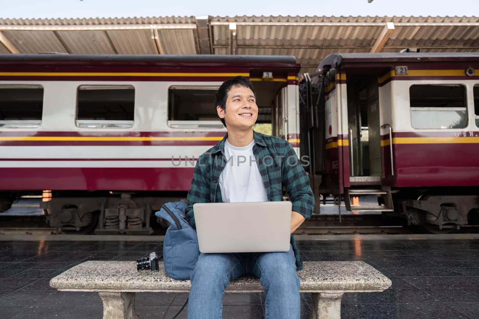 While waiting at the station, a man uses his laptop to work, combining travel with productivity in a modern lifestyle.