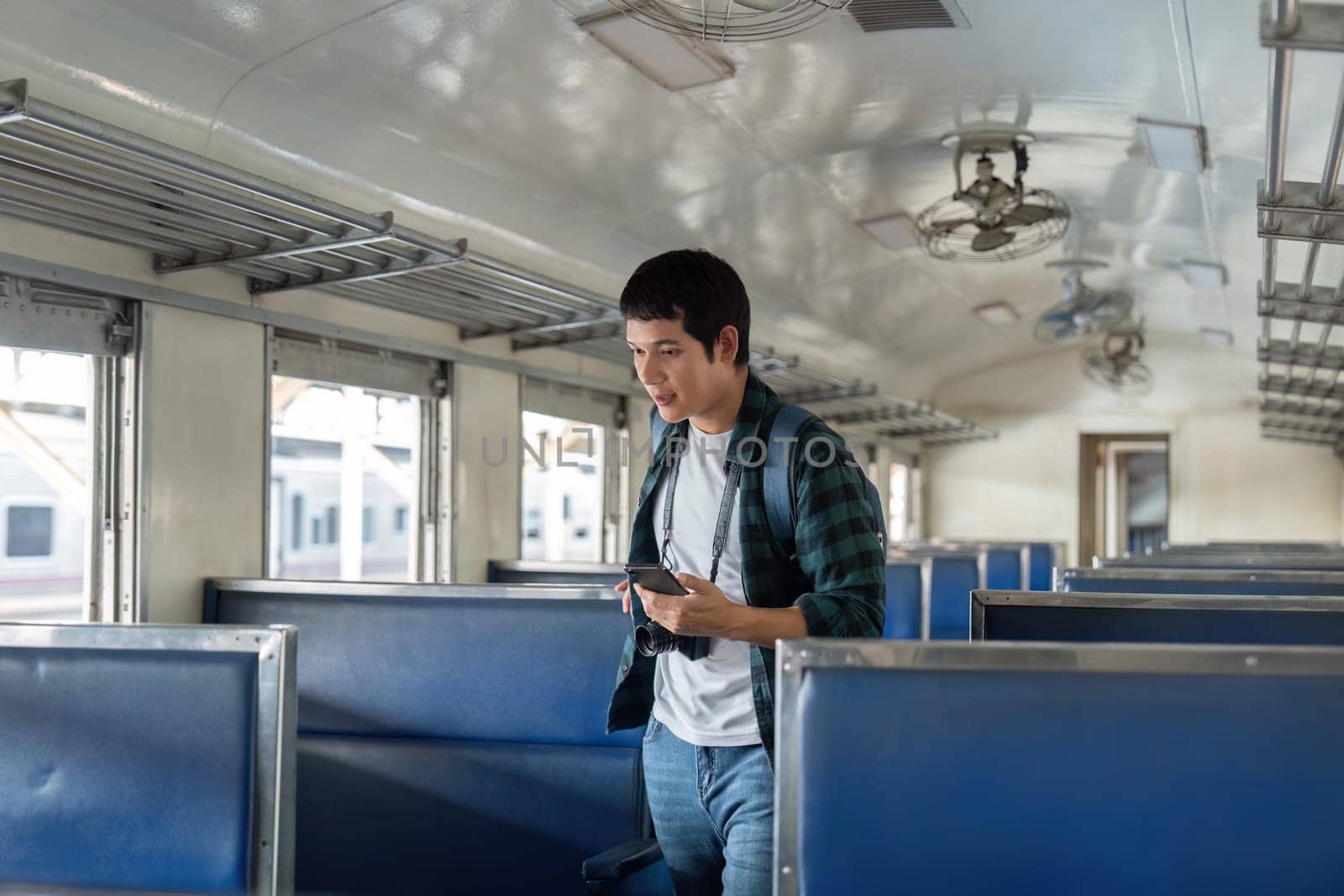 In the calm atmosphere of a train, a young traveler walks through the aisles, using his phone as a guide for his journey.