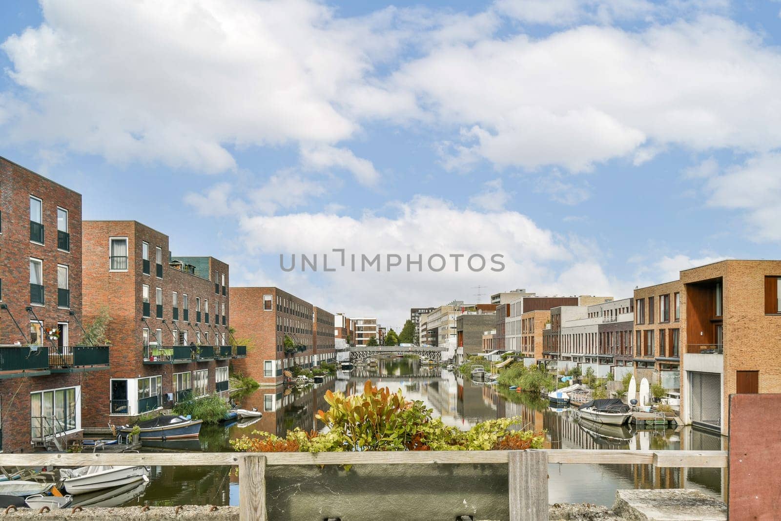 A picturesque view of a tranquil waterfront lined with modern residential buildings, lush greenery, and colorful reflections on the water under a cloudy sky.