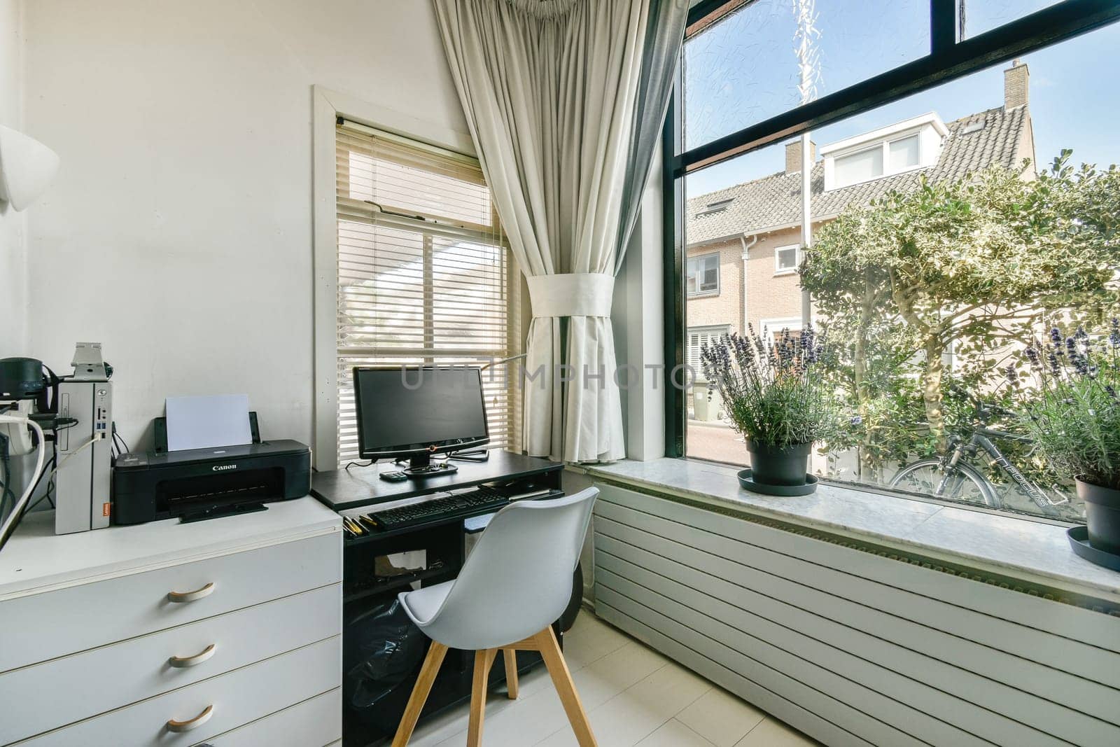 A well-lit home office featuring a computer on a desk, stylish chair, and large windows overlooking a garden, blending comfort and functionality seamlessly.