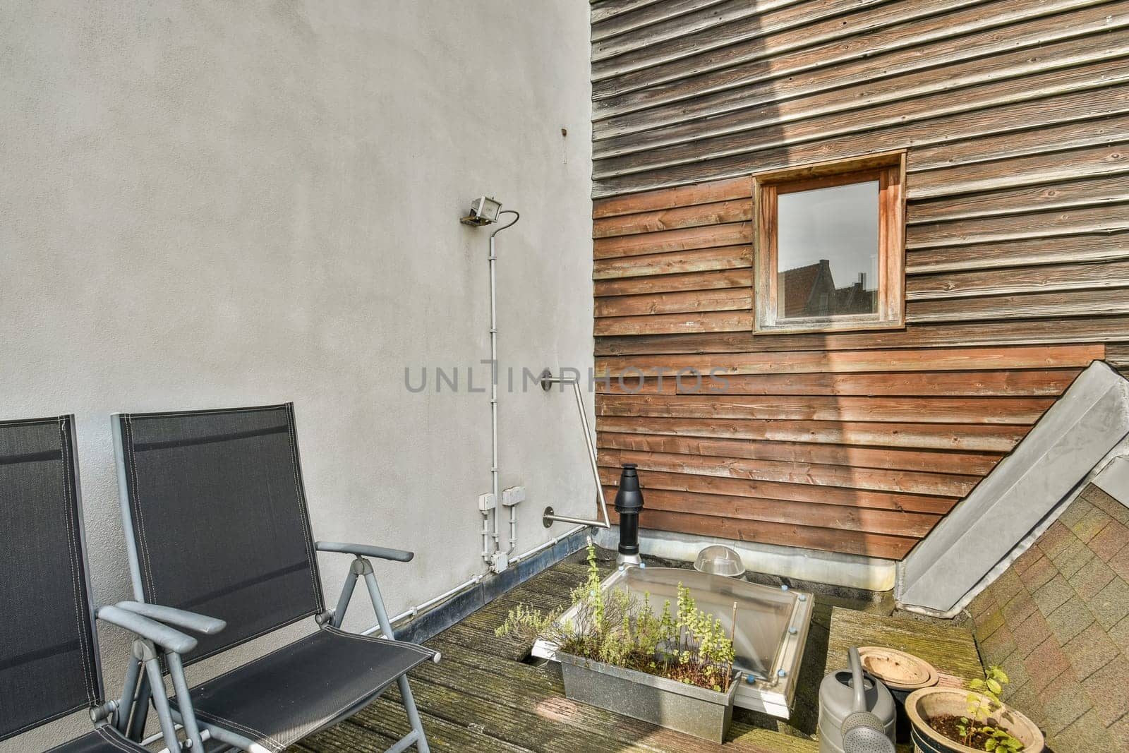 A serene outdoor patio featuring wooden walls, two chairs, and planters, perfect for relaxation and enjoying nature.