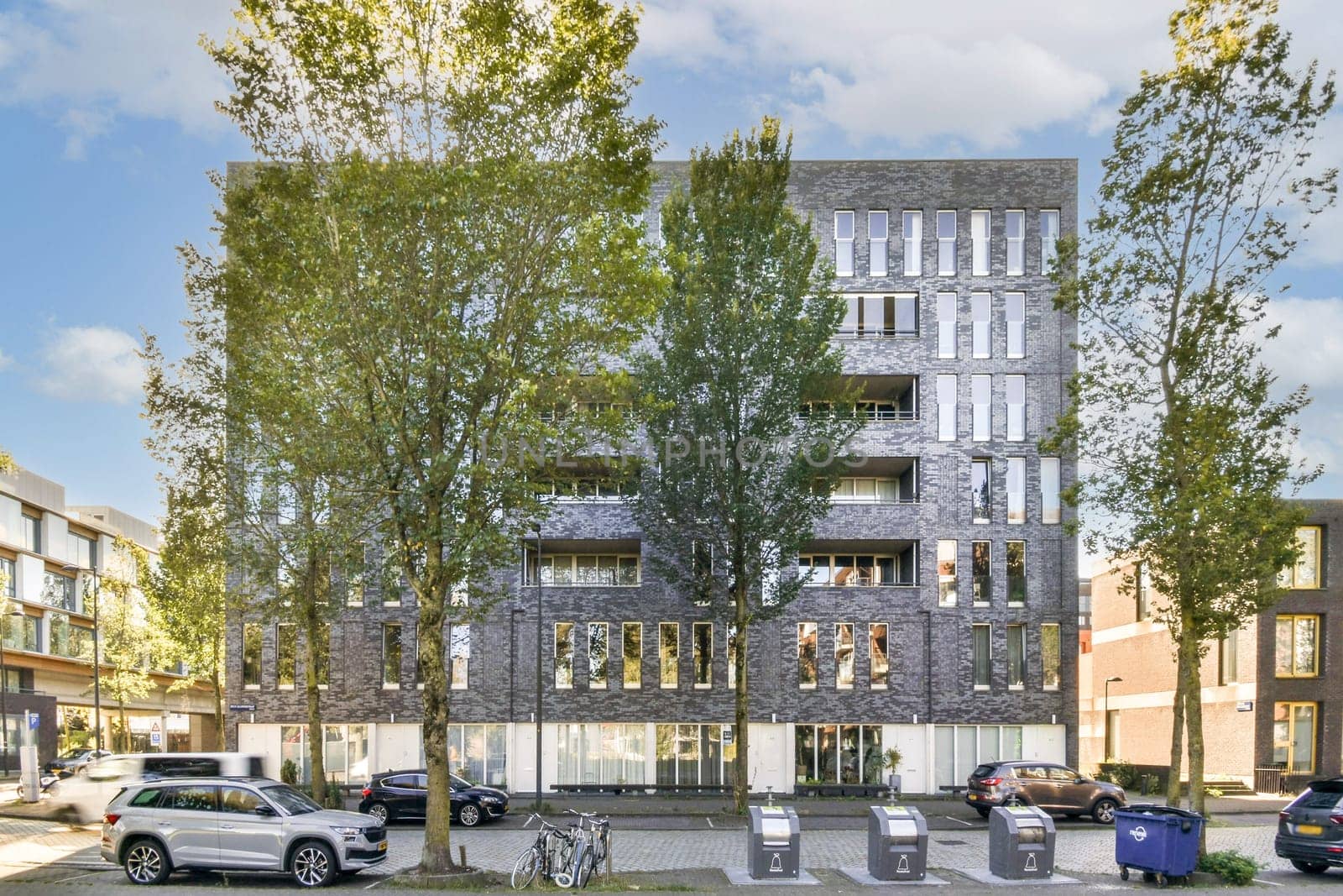 A sleek modern residential building features large windows and is framed by several trees, showcasing urban architecture harmonizing with nature.