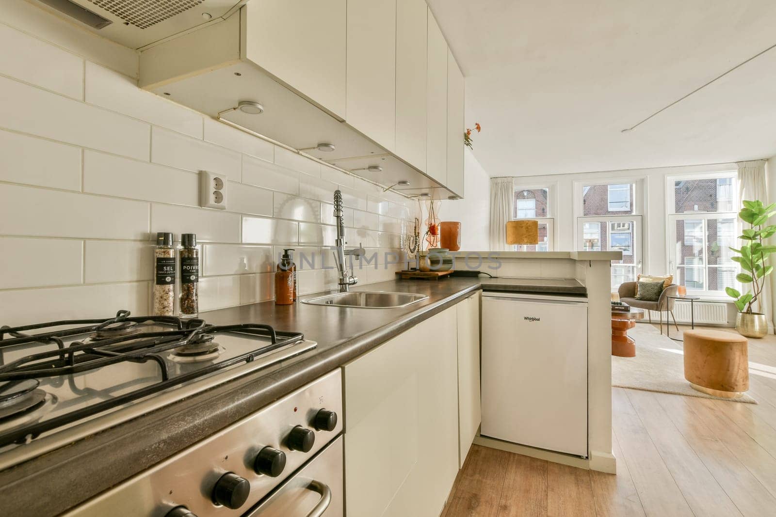 A bright modern kitchen featuring sleek cabinetry, stainless steel appliances, and a cozy seating area flooded with natural light from large windows.