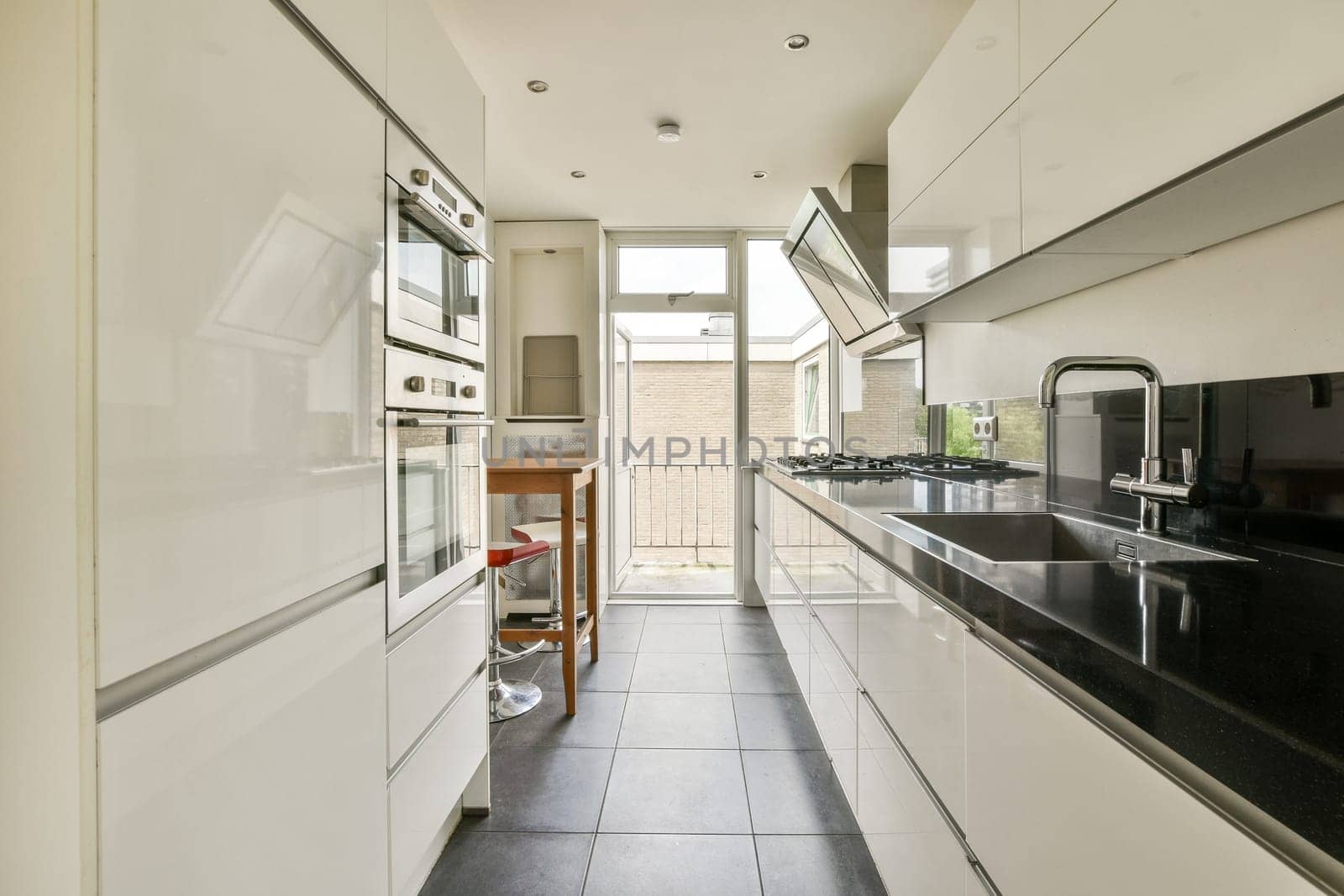 A sleek and modern kitchen featuring white cabinetry, black countertops, and ample natural light from large windows.