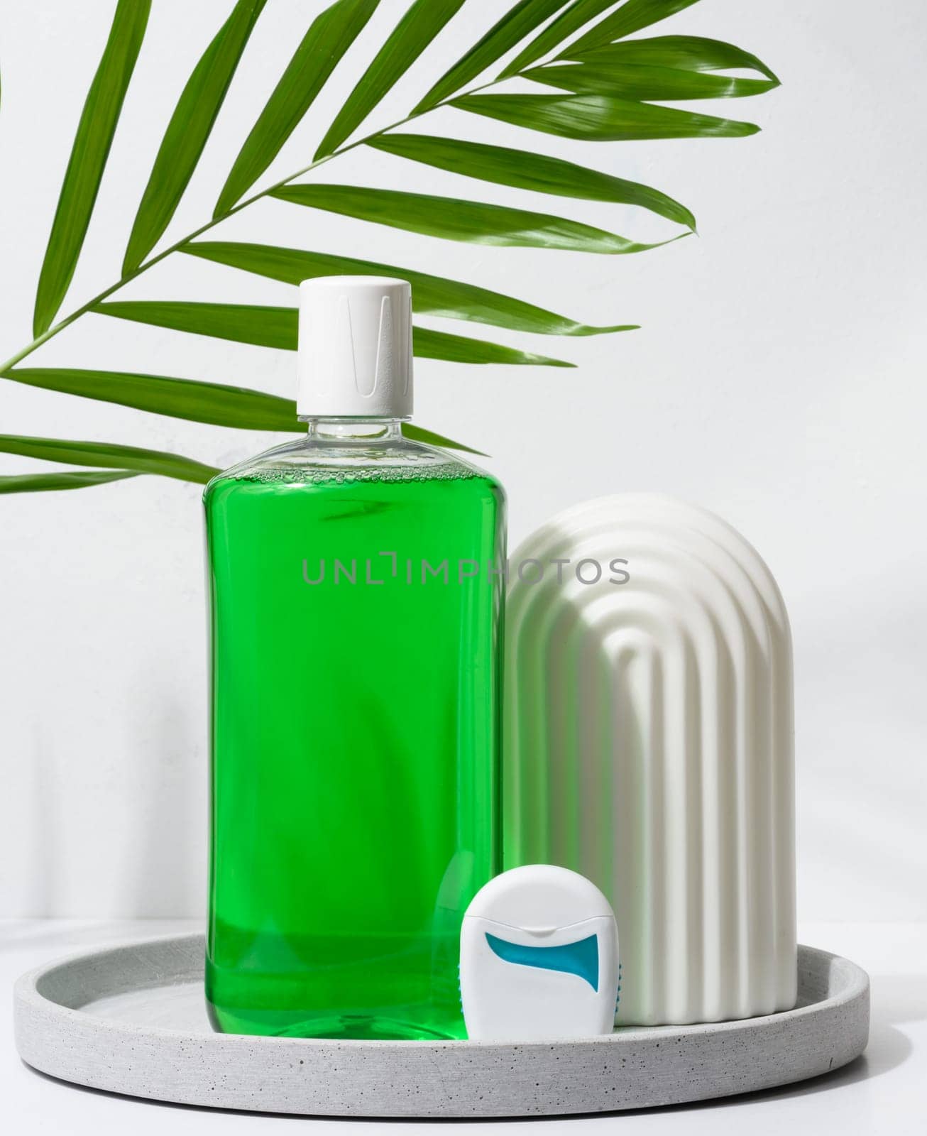 Refreshing mouthwash in a transparent plastic bottle and dental floss on a green background
