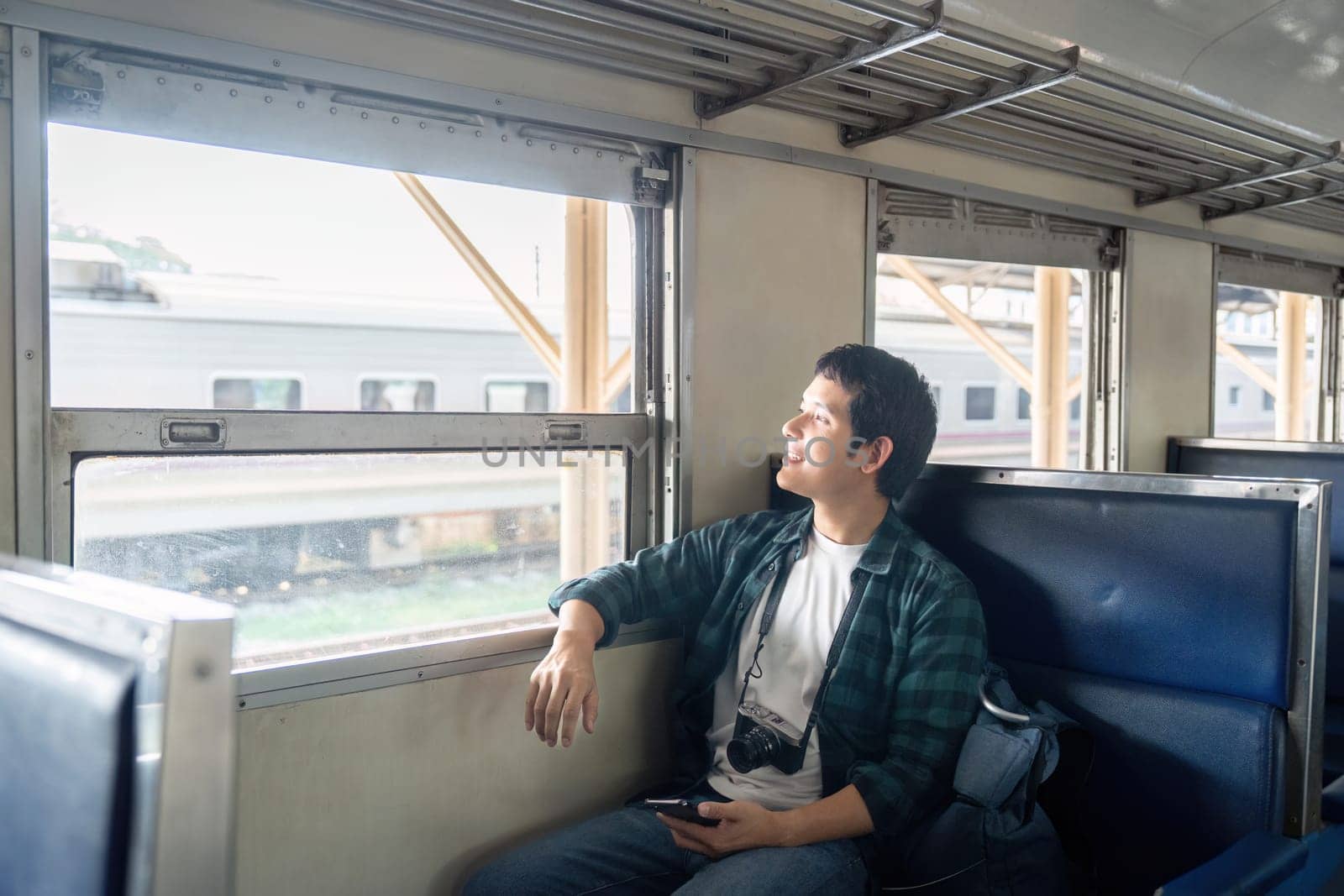 A young man sits on a train, looking out the window with a sense of wonder. He is likely contemplating his next destination and embracing the spirit of adventure.
