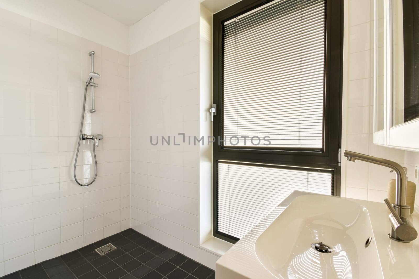 A stylish modern bathroom featuring sleek fixtures, a spacious shower area, and large windows allowing natural light. The minimalist aesthetic emphasizes clean lines and functionality.