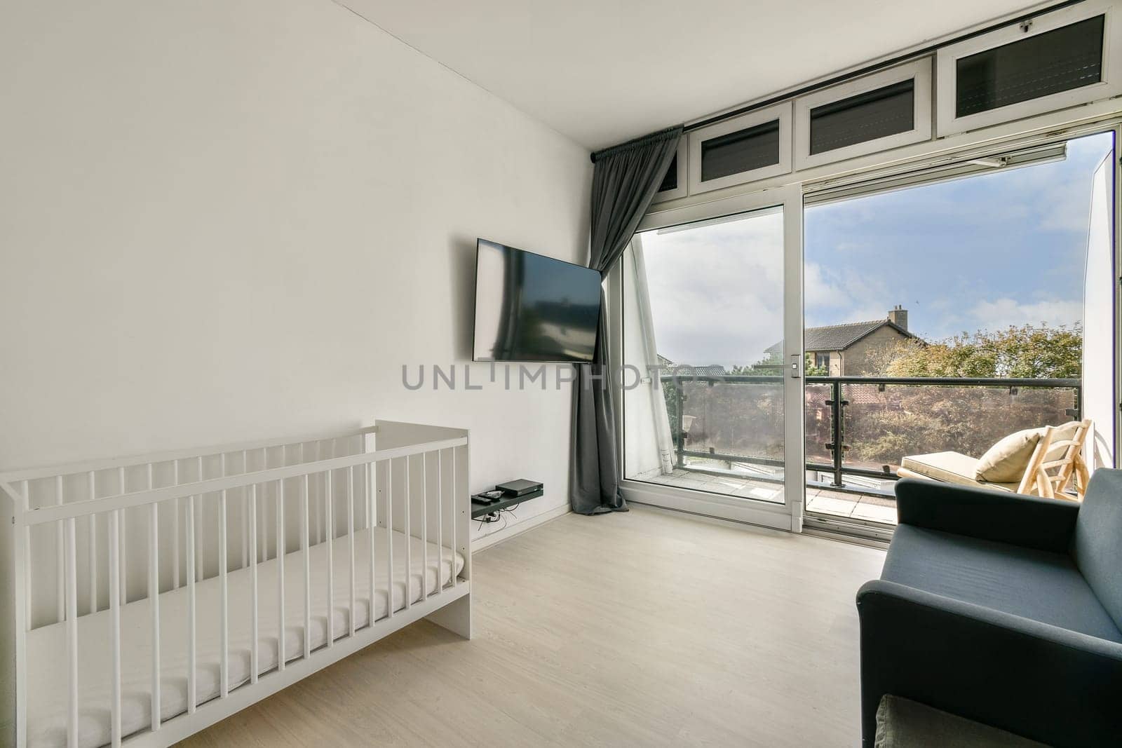 A bright and airy modern interior featuring a crib, sleek furnishings, and large windows that provide a view of the outdoors, enhancing the peaceful atmosphere.