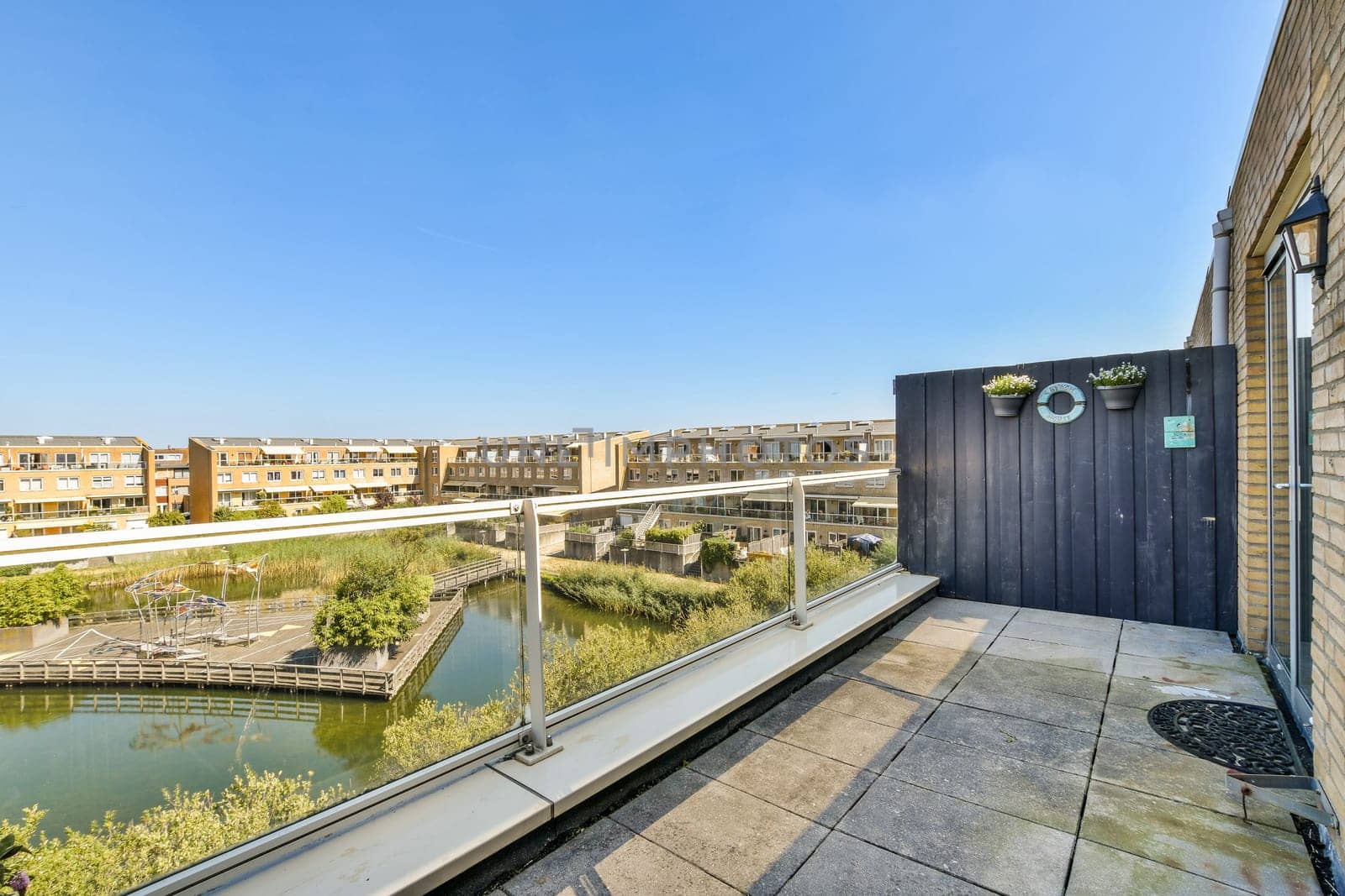 A modern residential balcony showcases a beautiful view of green landscapes, neatly designed buildings, and an inviting outdoor space under a clear blue sky.