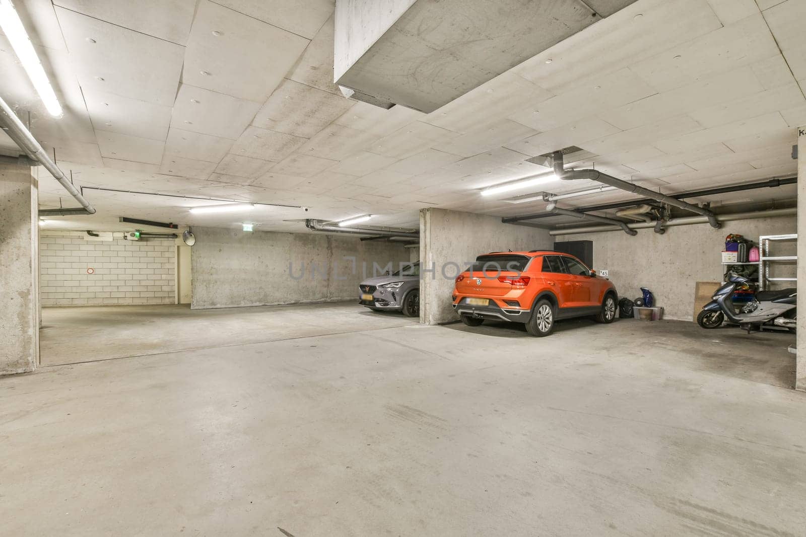 A spacious and well-lit underground parking garage featuring two parked vehicles. The modern architecture emphasizes clean lines and functionality.