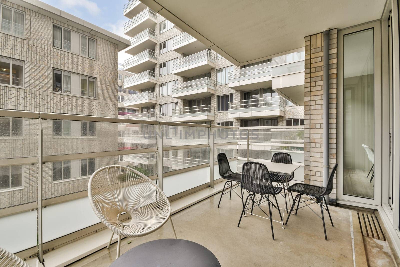 A stylish balcony showcasing contemporary architecture and city living, featuring glass railings and minimalist furniture under a clear sky.