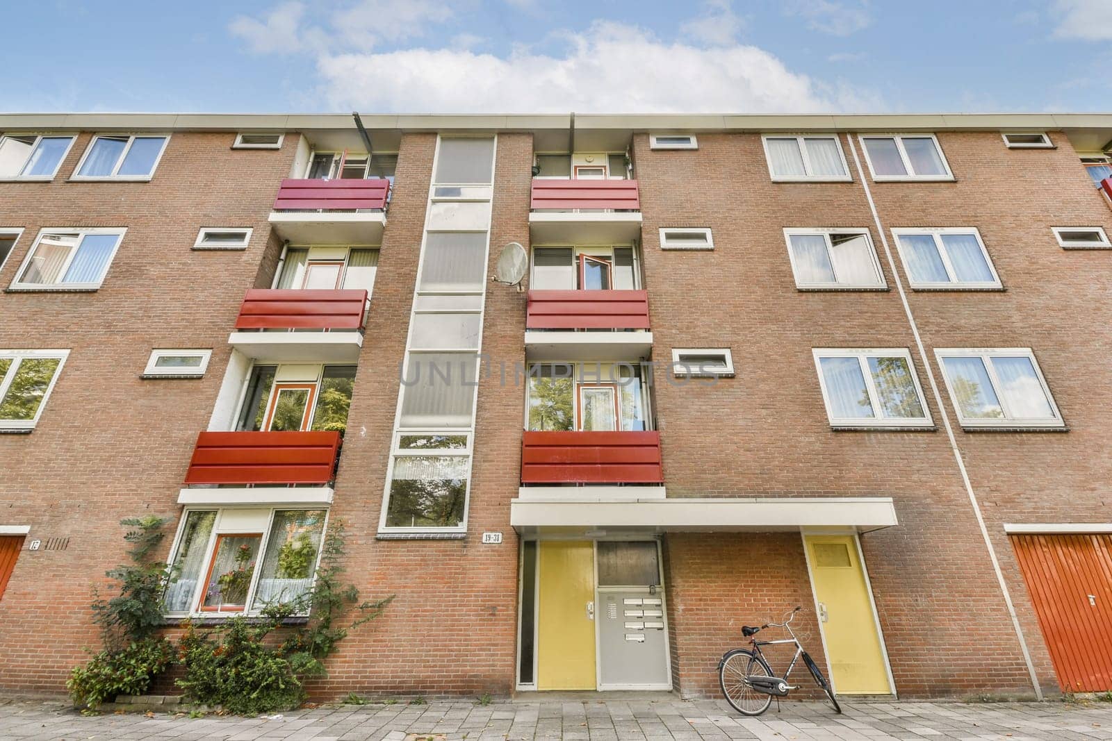 A contemporary residential building featuring vibrant balconies, large windows, and a sleek entrance, set in an urban neighborhood with lush greenery.