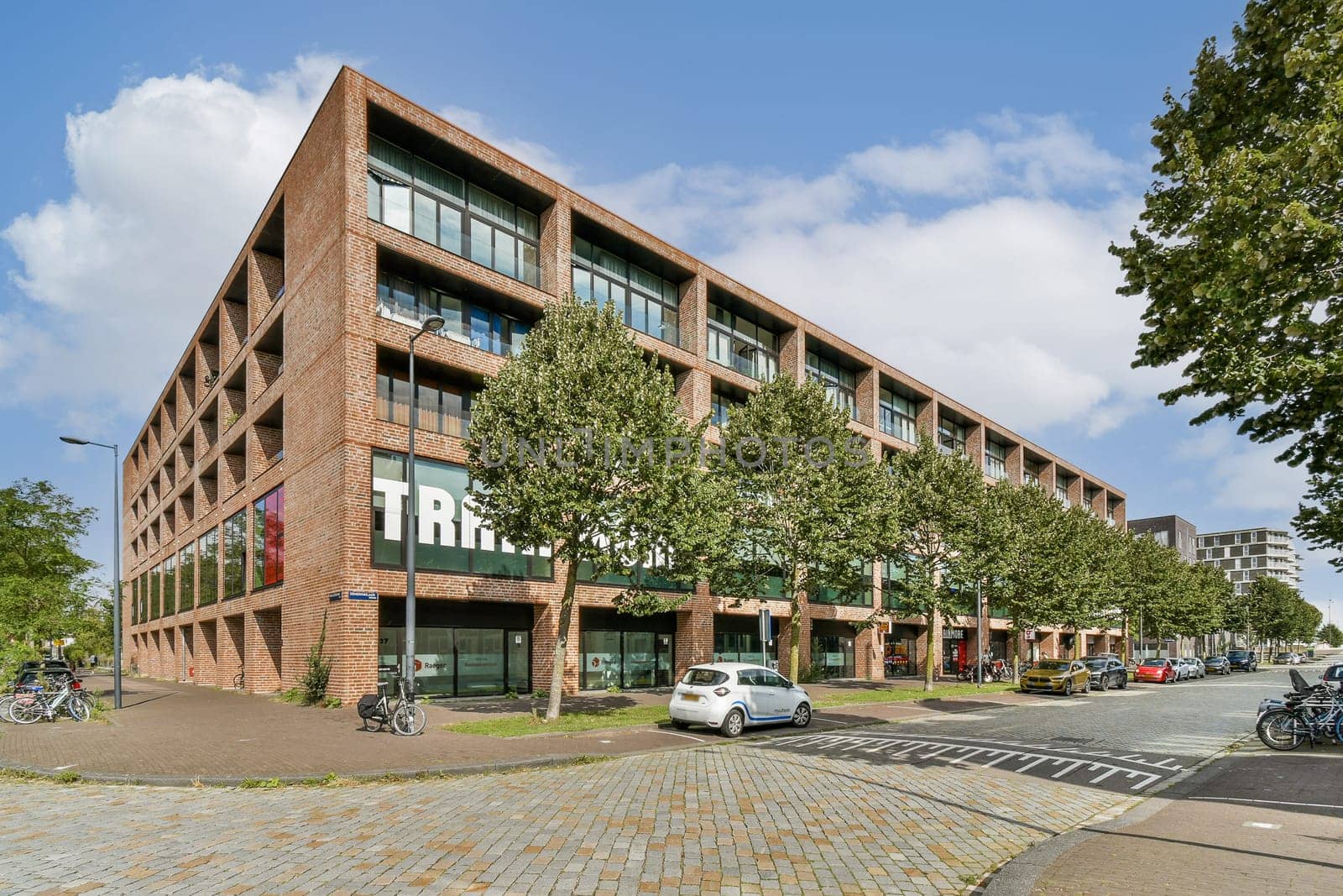 A contemporary office structure featuring a brick facade and ample greenery. The design integrates nature with urban architecture, emphasizing sustainability.