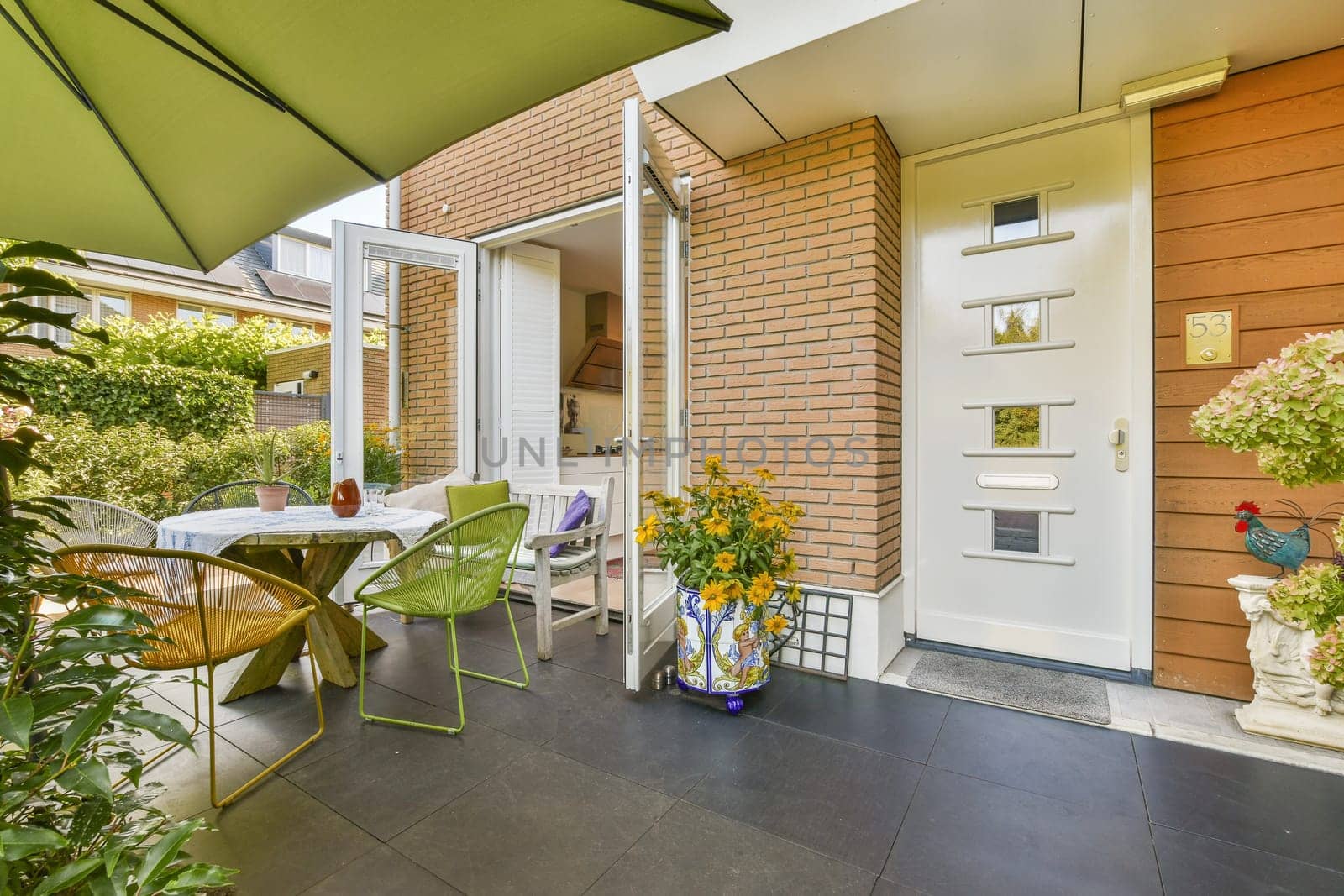 A welcoming entryway featuring a modern door, stylish outdoor seating, and vibrant plants, creating an inviting atmosphere for visitors.