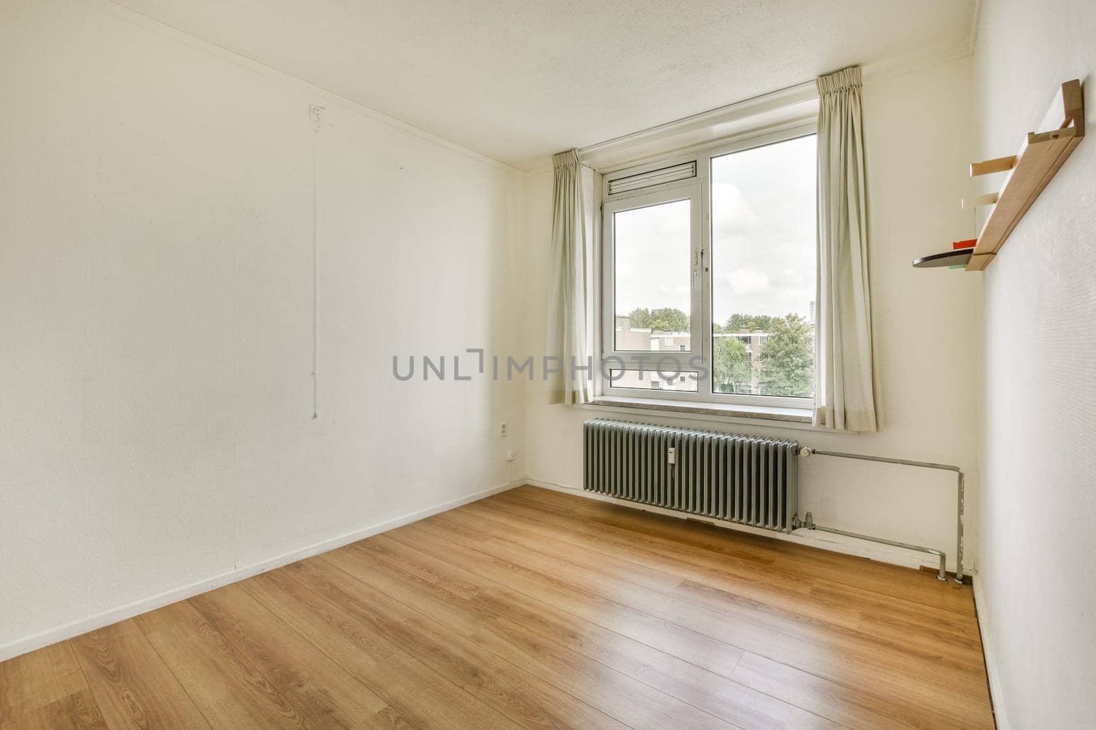 An uncluttered interior room featuring smooth wooden flooring, a large window allowing natural light, and minimal furnishings, perfect for modern living.