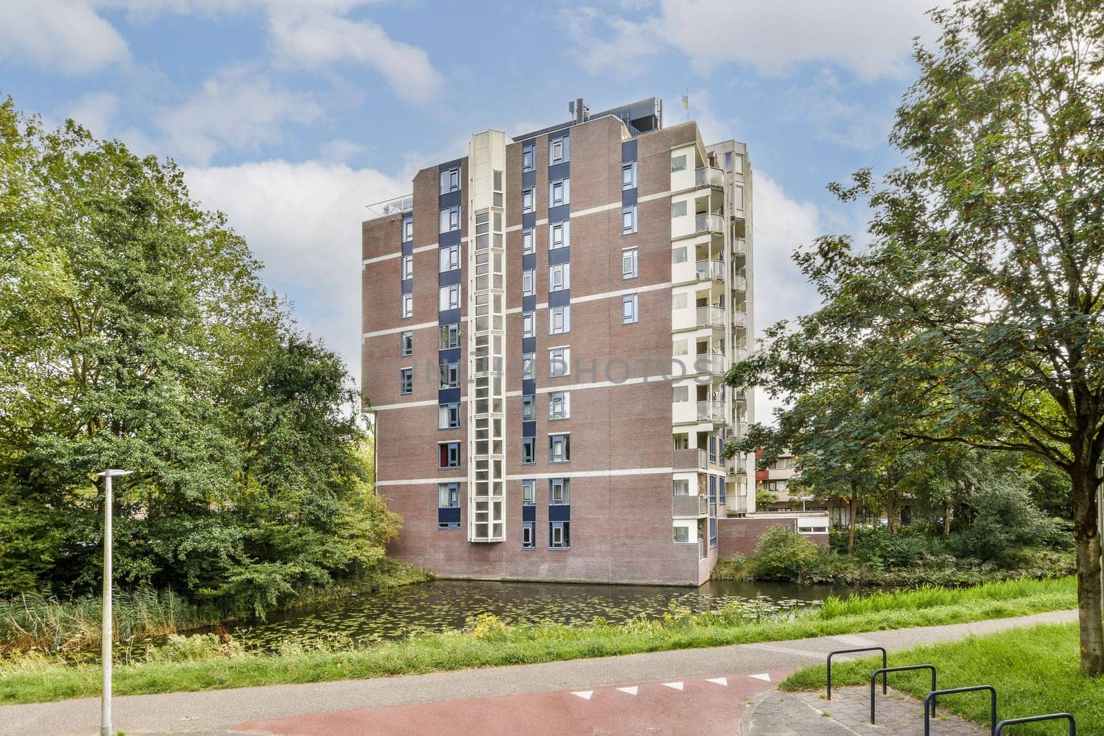 A stylish modern residential building stands beside a serene waterway, encircled by lush greenery and trees, showcasing contemporary architecture.