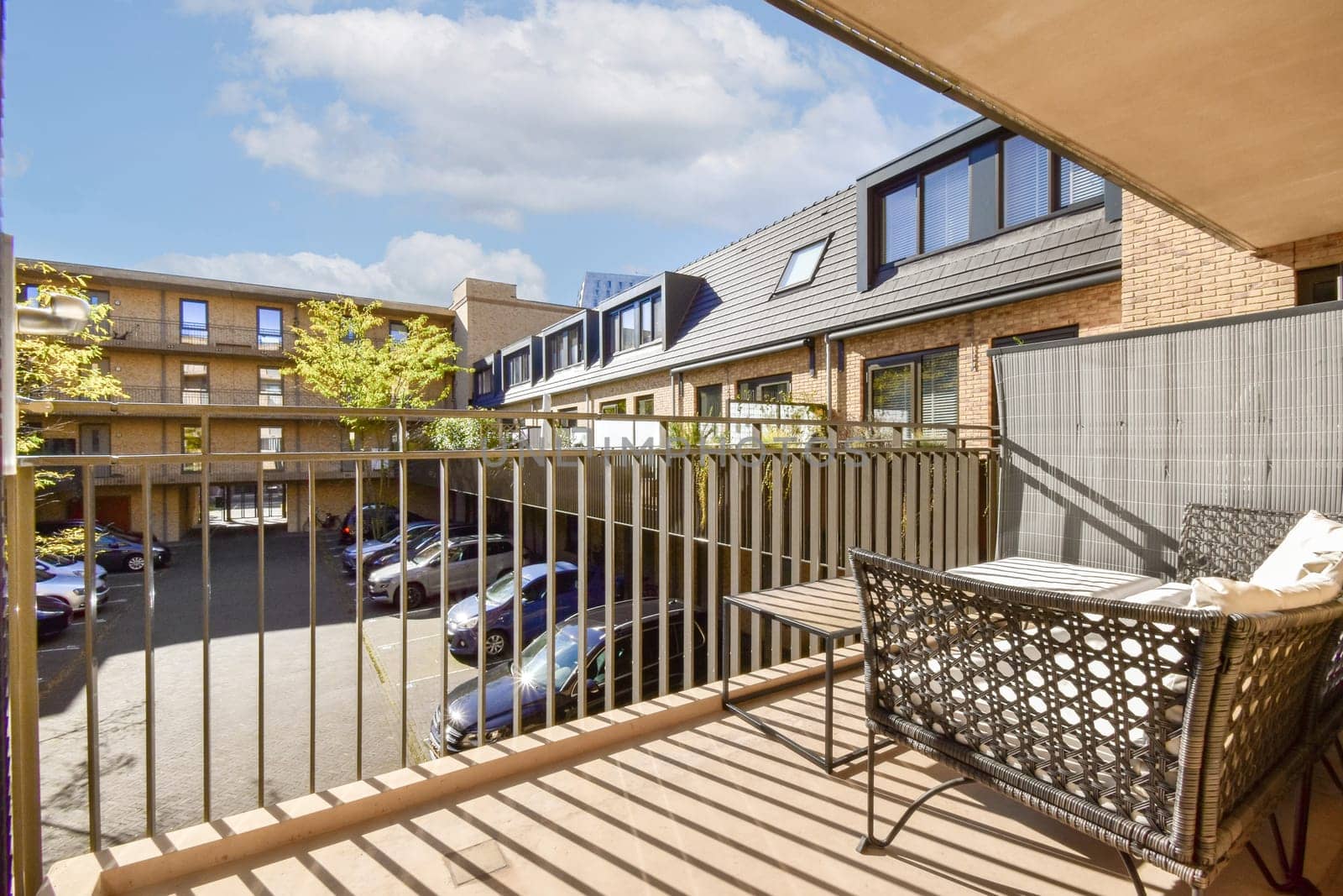A stylish balcony showcasing modern architecture with a view of an urban courtyard and parked cars. Natural light highlights the contemporary design elements.