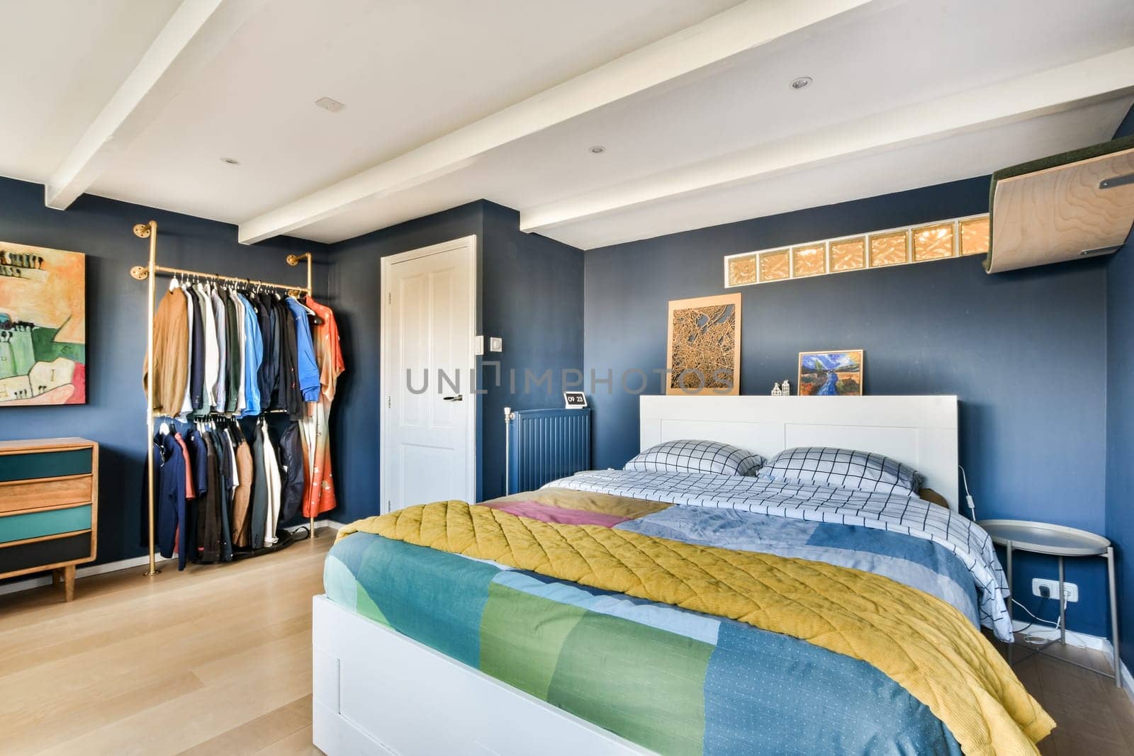 A stylish modern bedroom featuring a neatly made bed, a colorful blanket, and organized clothing in a wardrobe. The decor is contemporary and inviting.