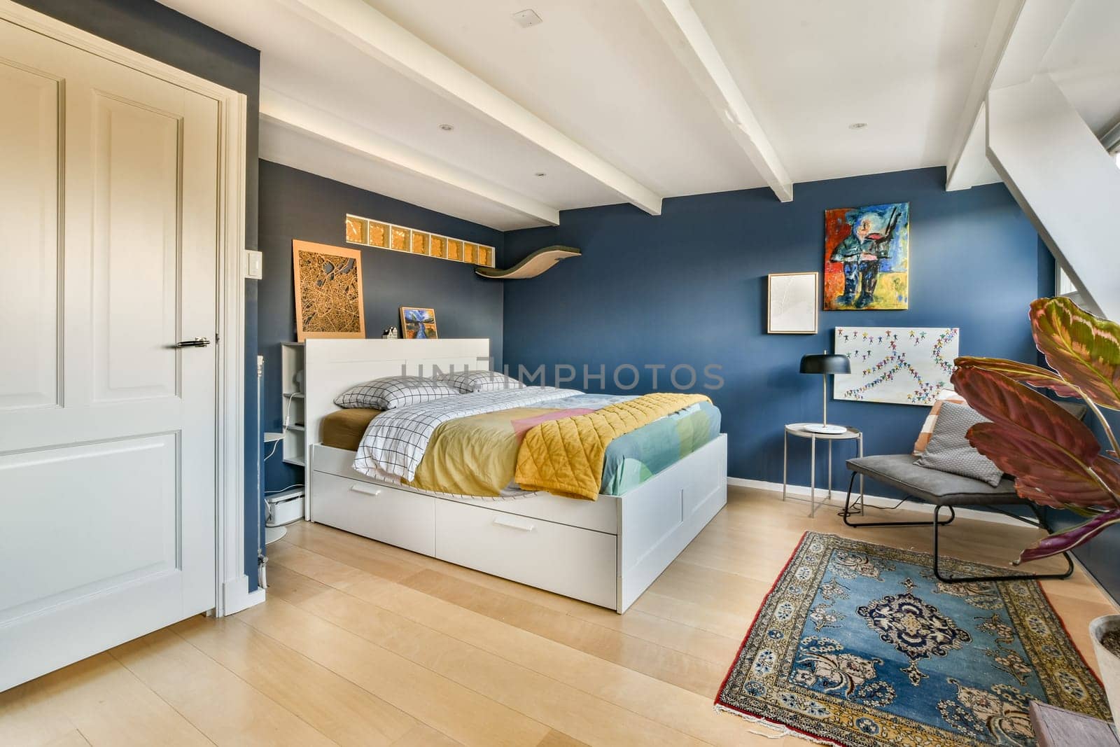 Stylish bedroom featuring a blue accent wall, cozy bed with colorful bedding, and contemporary decor elements creating a serene atmosphere.