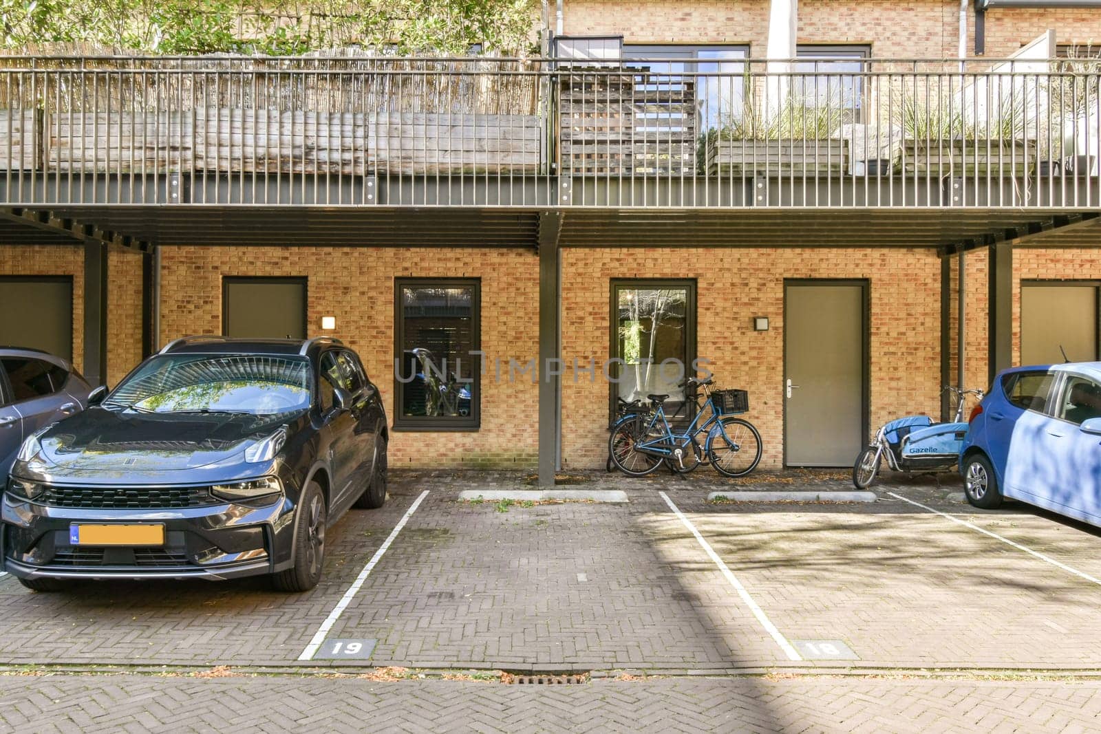 A well-lit parking area showcasing a modern vehicle and a bicycle. The layout features multiple parking spaces beside a building with enhanced greenery.